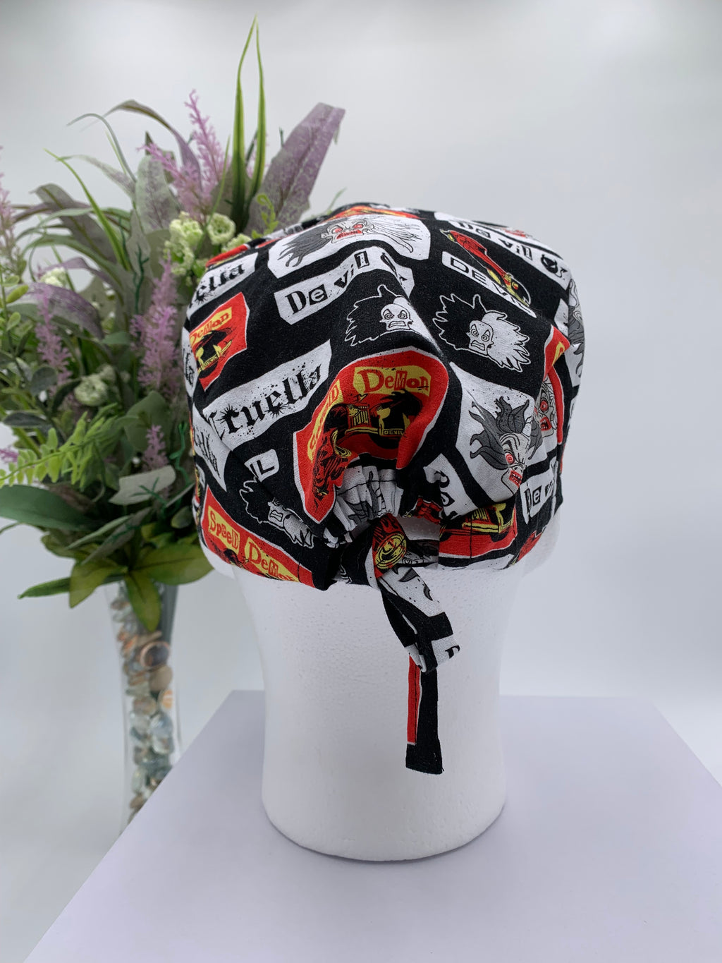 Mannequin head wearing a Cruella DeVil scrub cap with a decorative plant in the background.