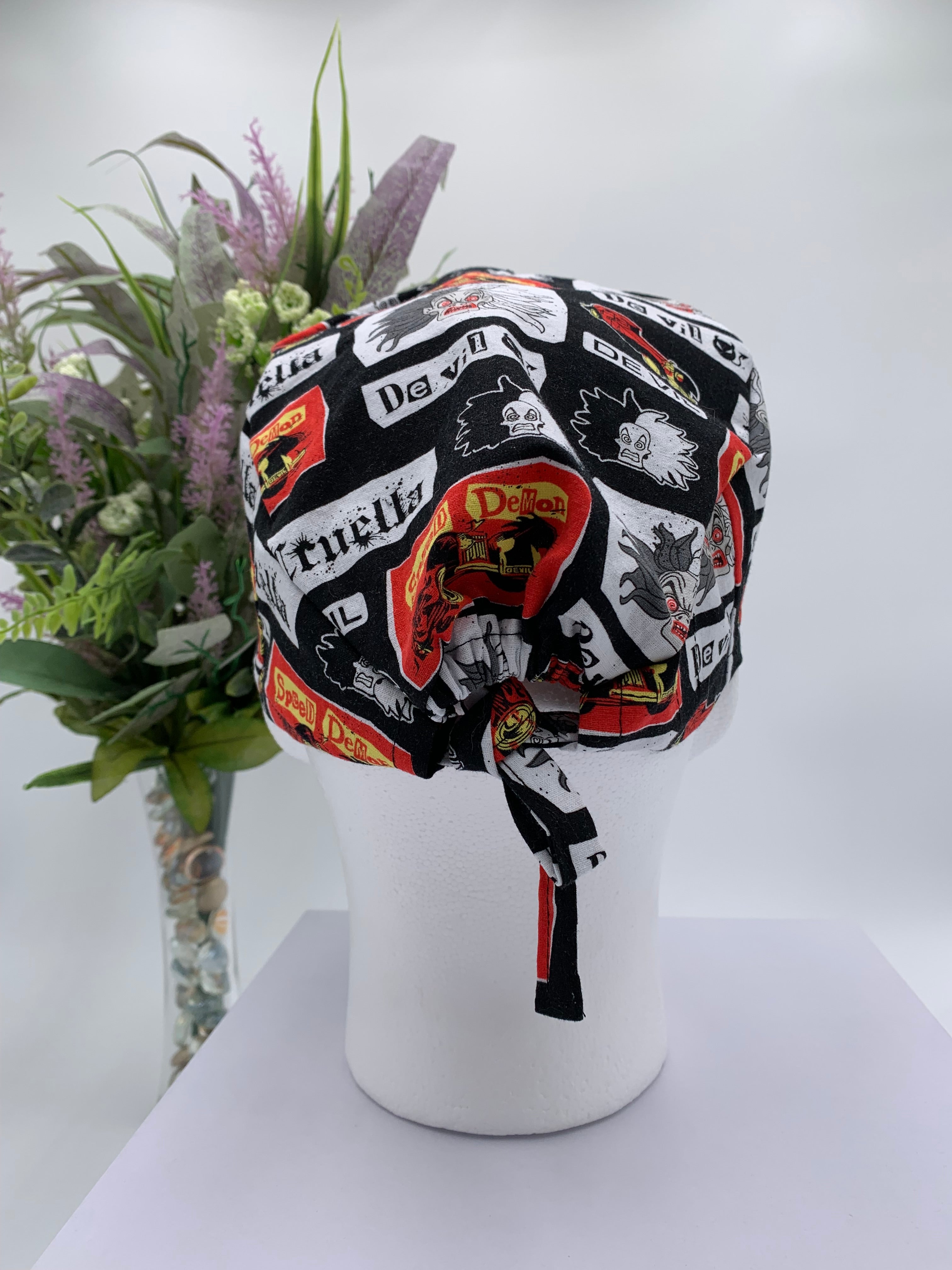 Mannequin head wearing a Cruella DeVil scrub cap with a decorative plant in the background.