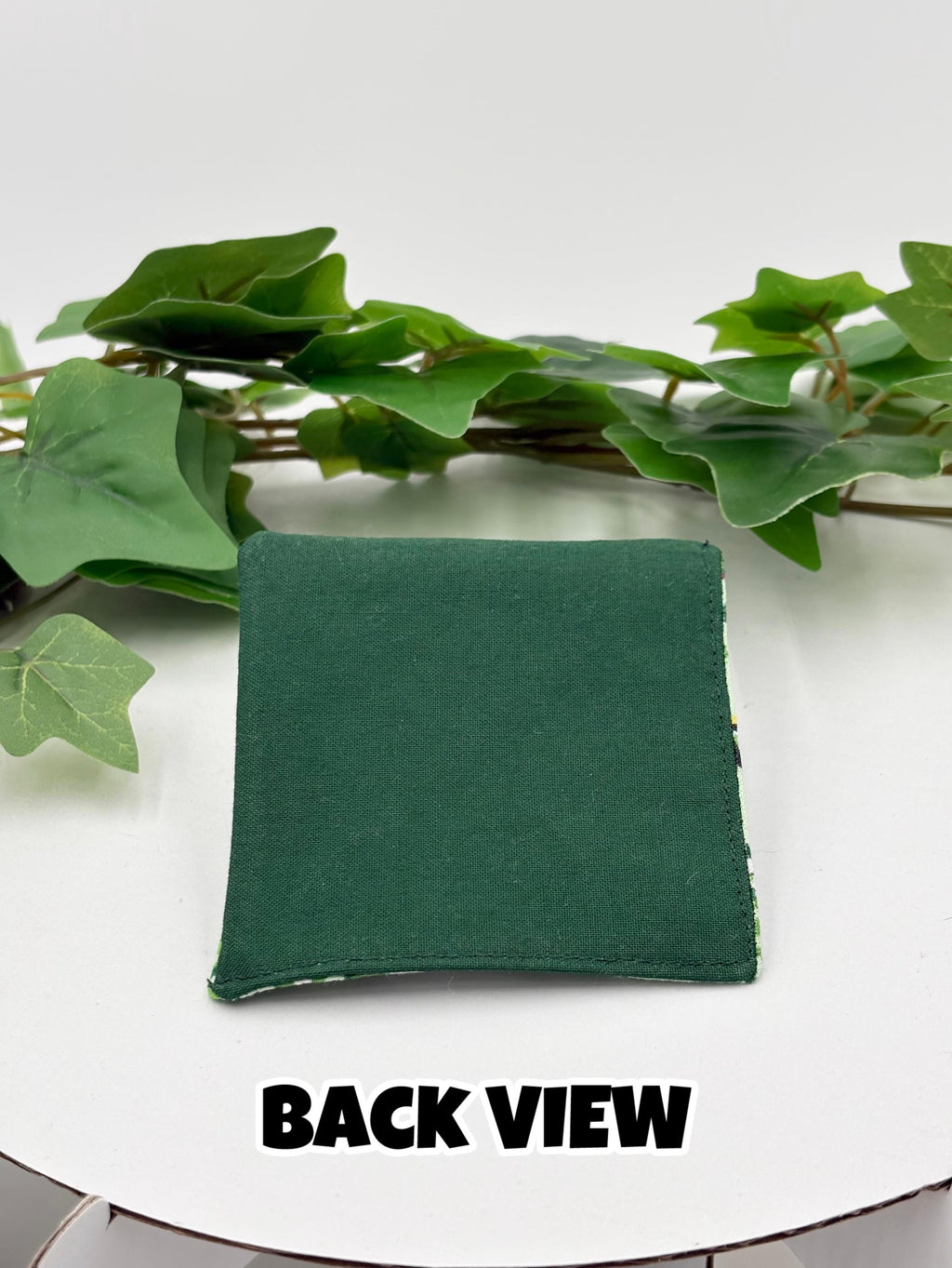 Green fabric square corner bookmark on a white surface with green leaves in the background with text "back view"