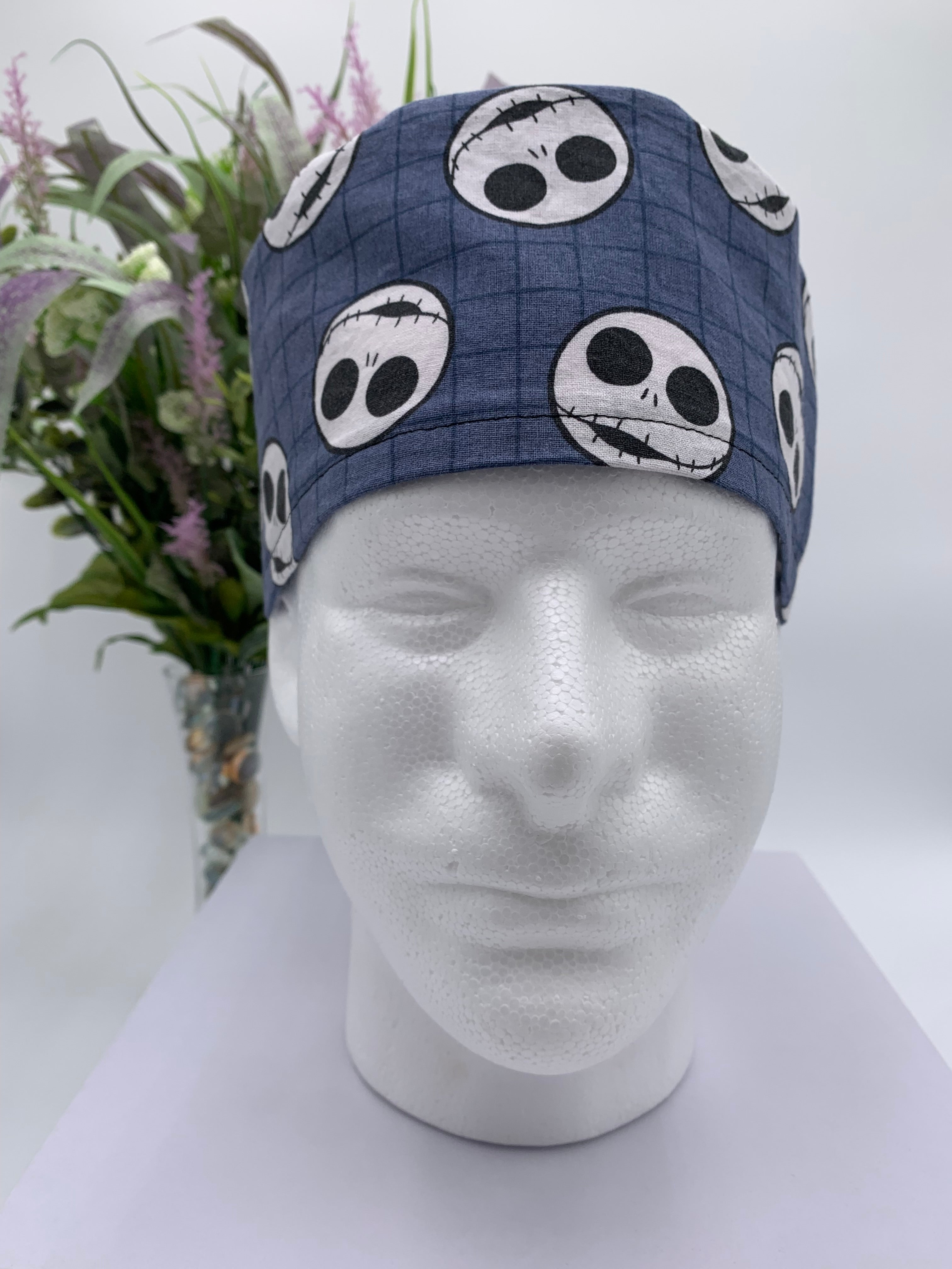Mannequin head wearing a jack skellington scrub cap with a decorative plant in the background.