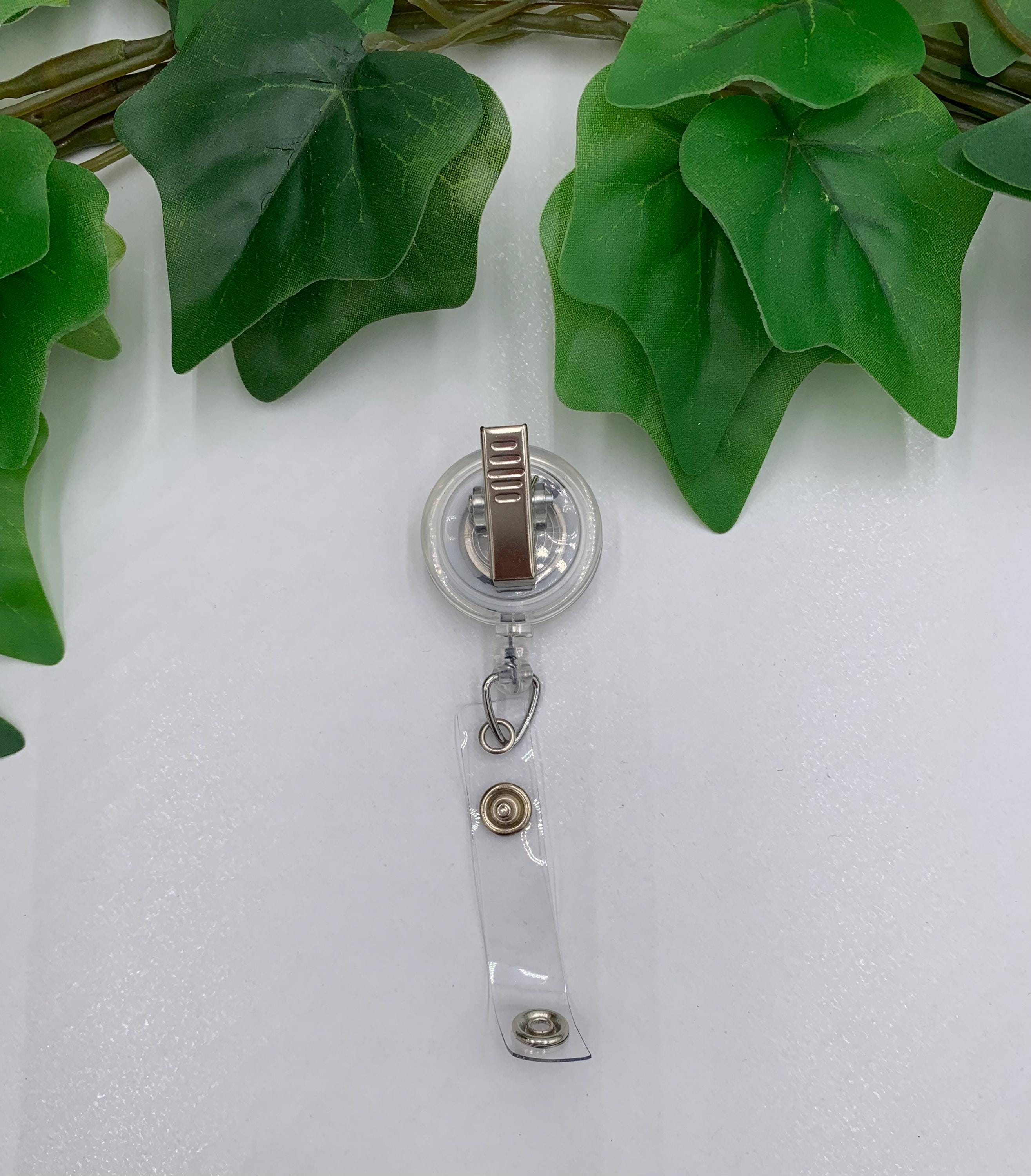 Clear badge holder with brown clip against a white background with green leaves.