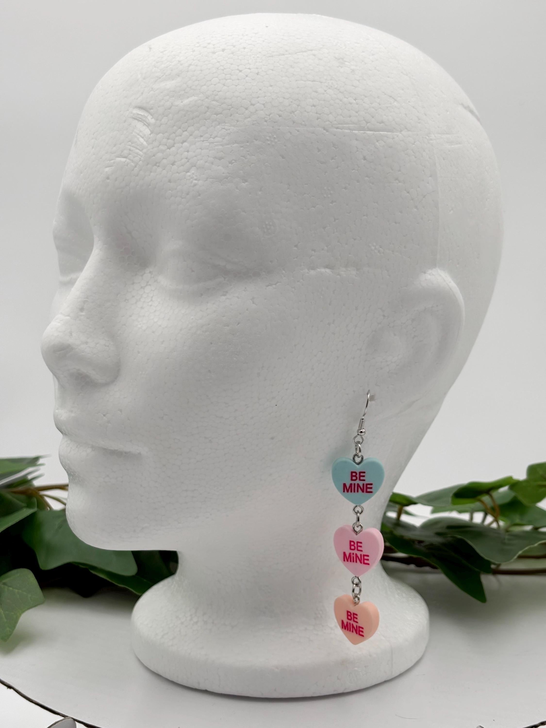 Heart-shaped dangle earrings on a mannequin head with green leaves in the background