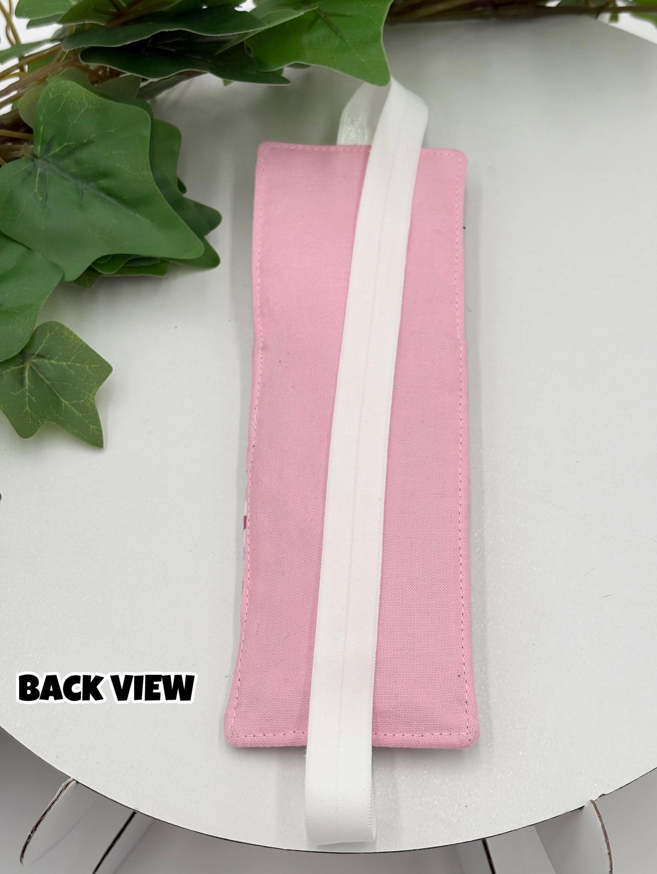 Pink pen holder bookmark with white strap on a white background with green leaves.