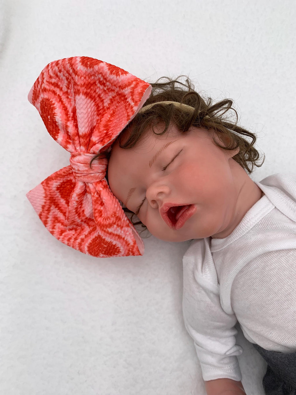 Newborn baby doll wearing a Pink Nylon Headband with a decorative hearts themed big bow on a mannequin head silhouette against a white background