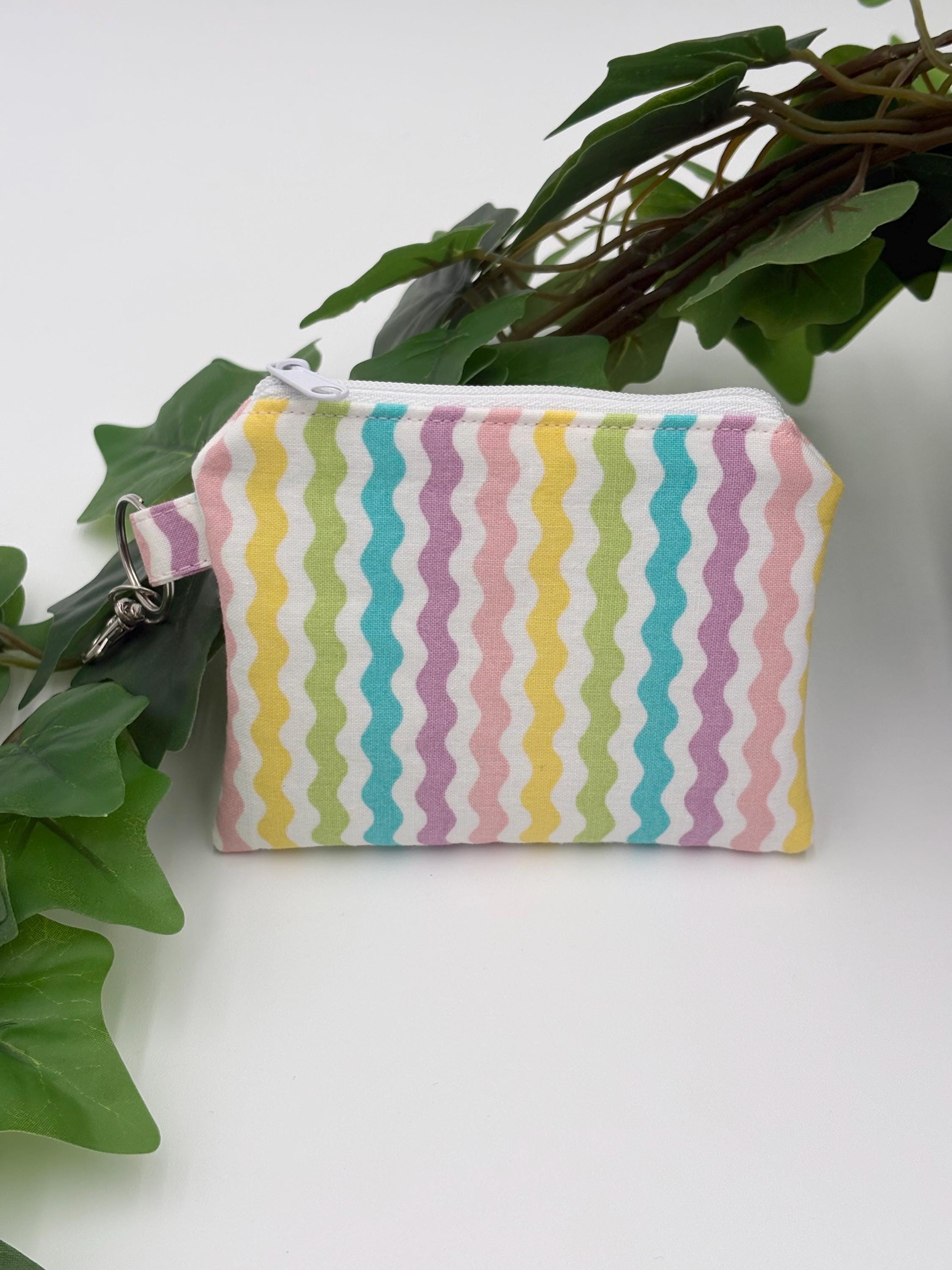 Small coin purse keychain with pastel zigzag pattern on a white background with green leaves 