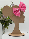 Pink Breast Cancer awareness themed big bow nylon headband on a mannequin head with a white background and greenery 