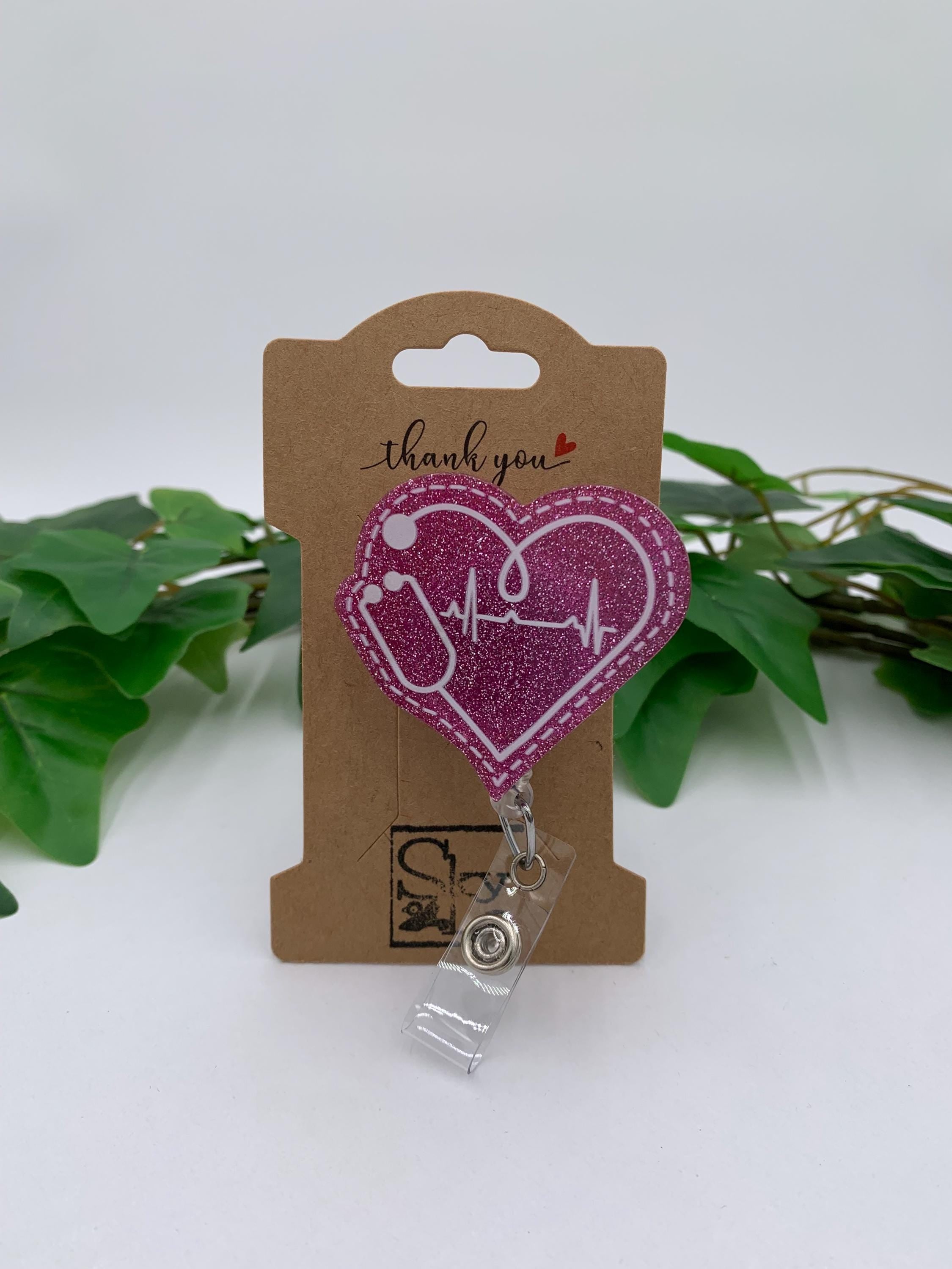 Heart-shaped badge holder with a clip on a 'thank you' card with green leaves in the background