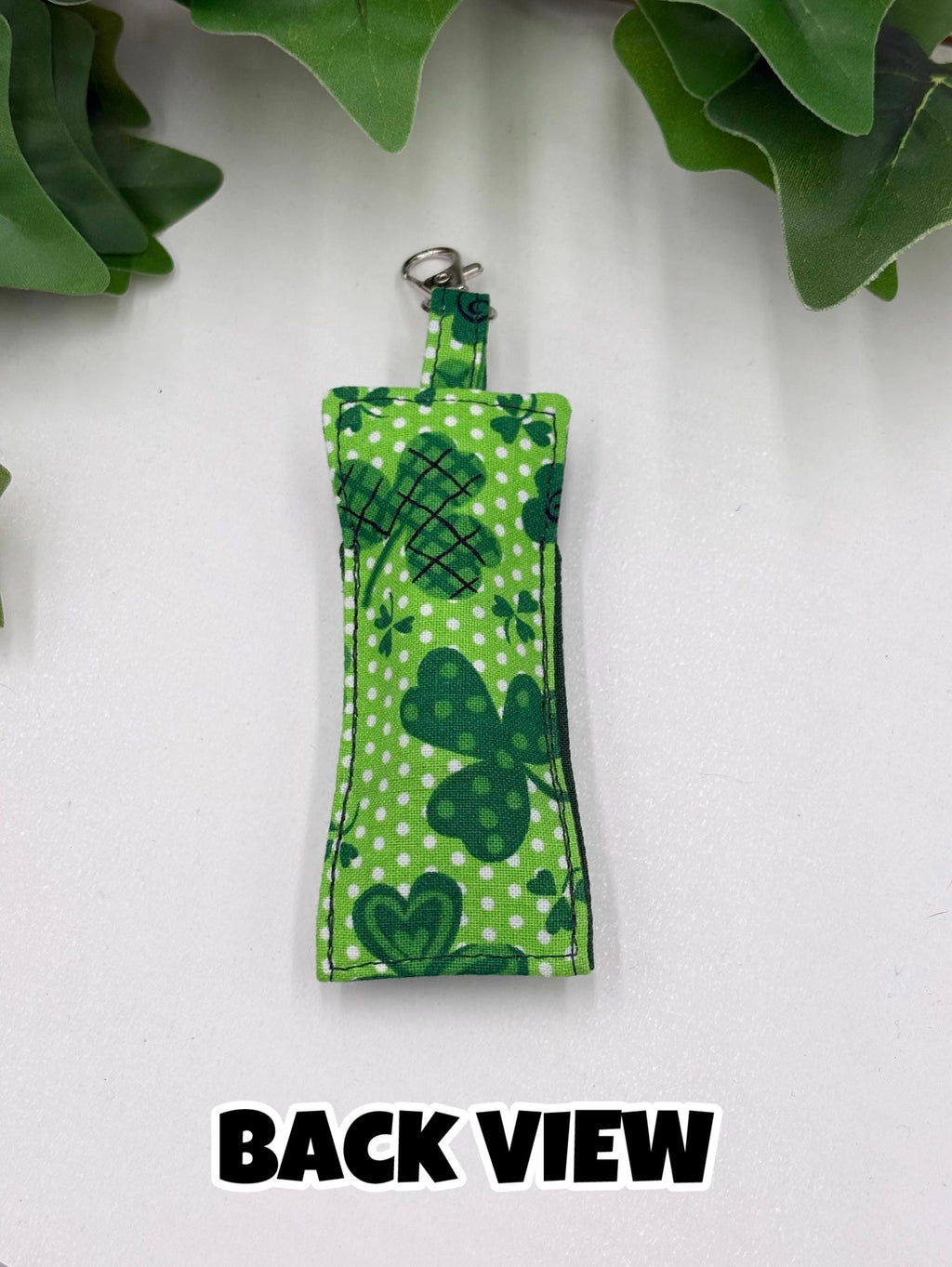 back view of Green shamrock-patterned chapstick holder on a white surface with green leaves in the background with text "back view"