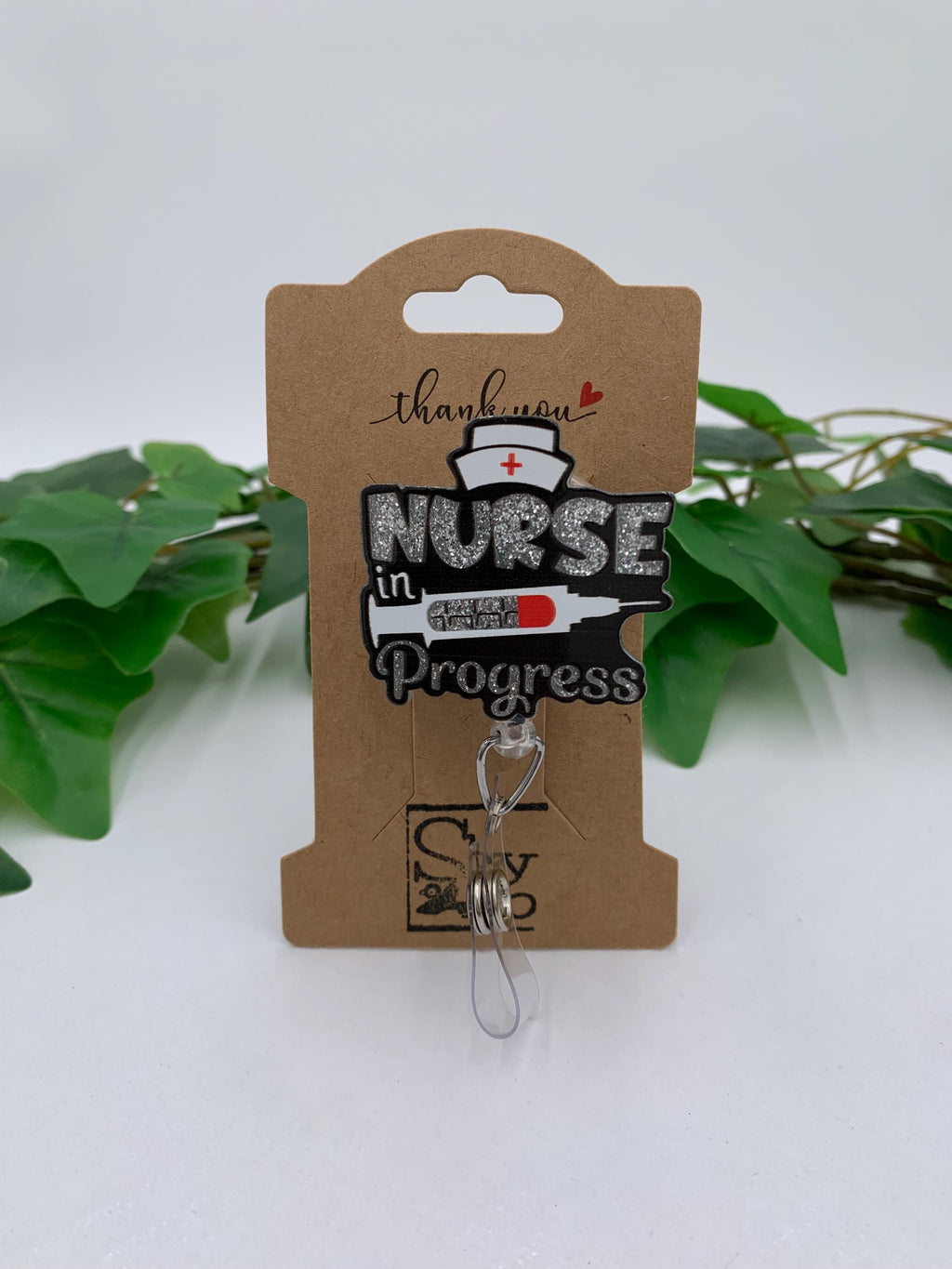Nurse in Progress badge reel on a cardboard backing with green leaves in the background