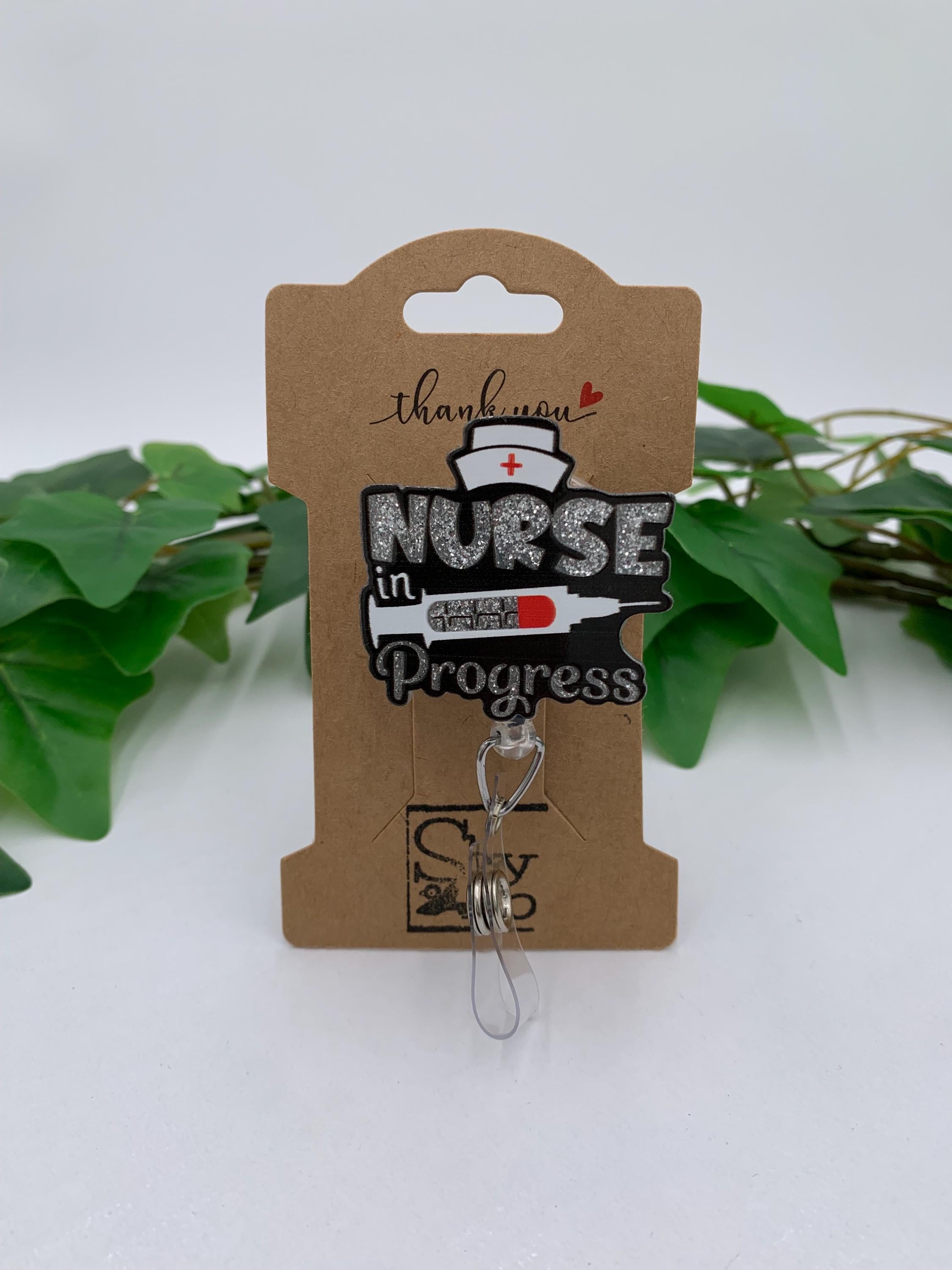 Nurse in Progress badge reel on a cardboard backing with green leaves in the background