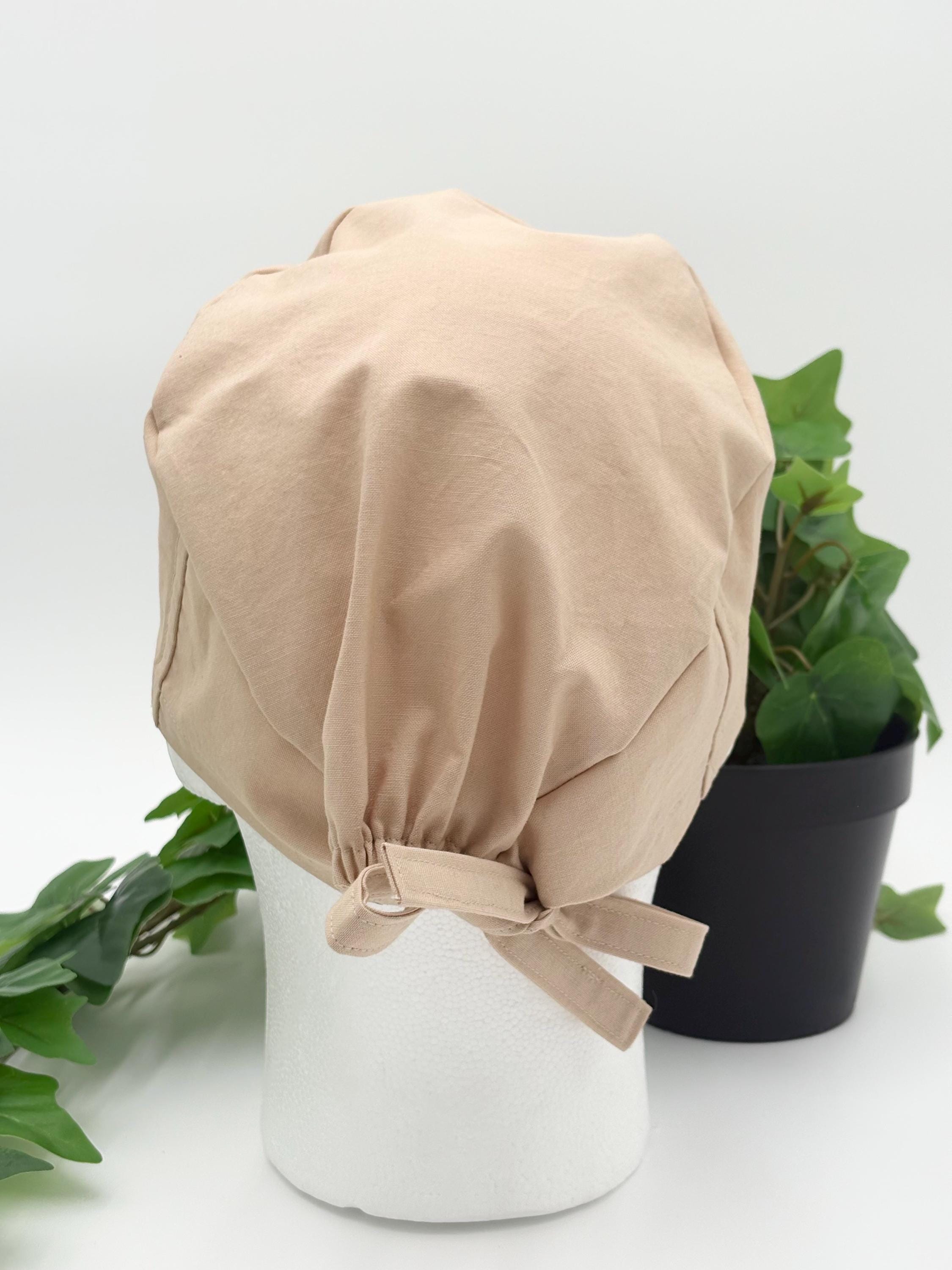 Beige scrub cap on a mannequin head with green plants in the background