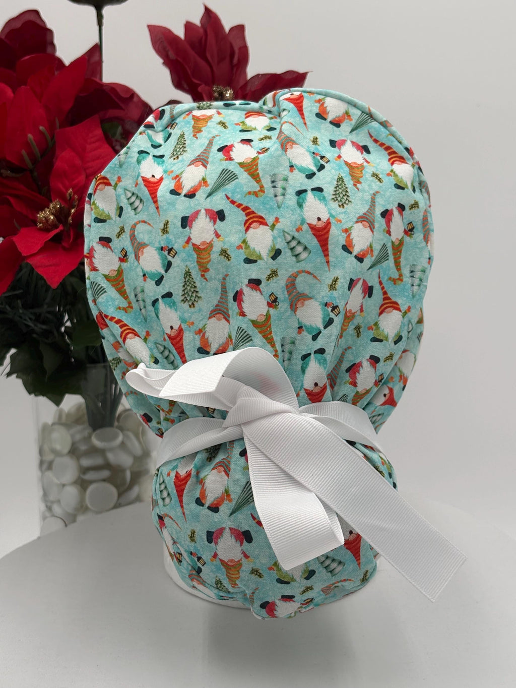 Gnomes scrub cap with ribbon on a mannequin head against a white background with red flowers.