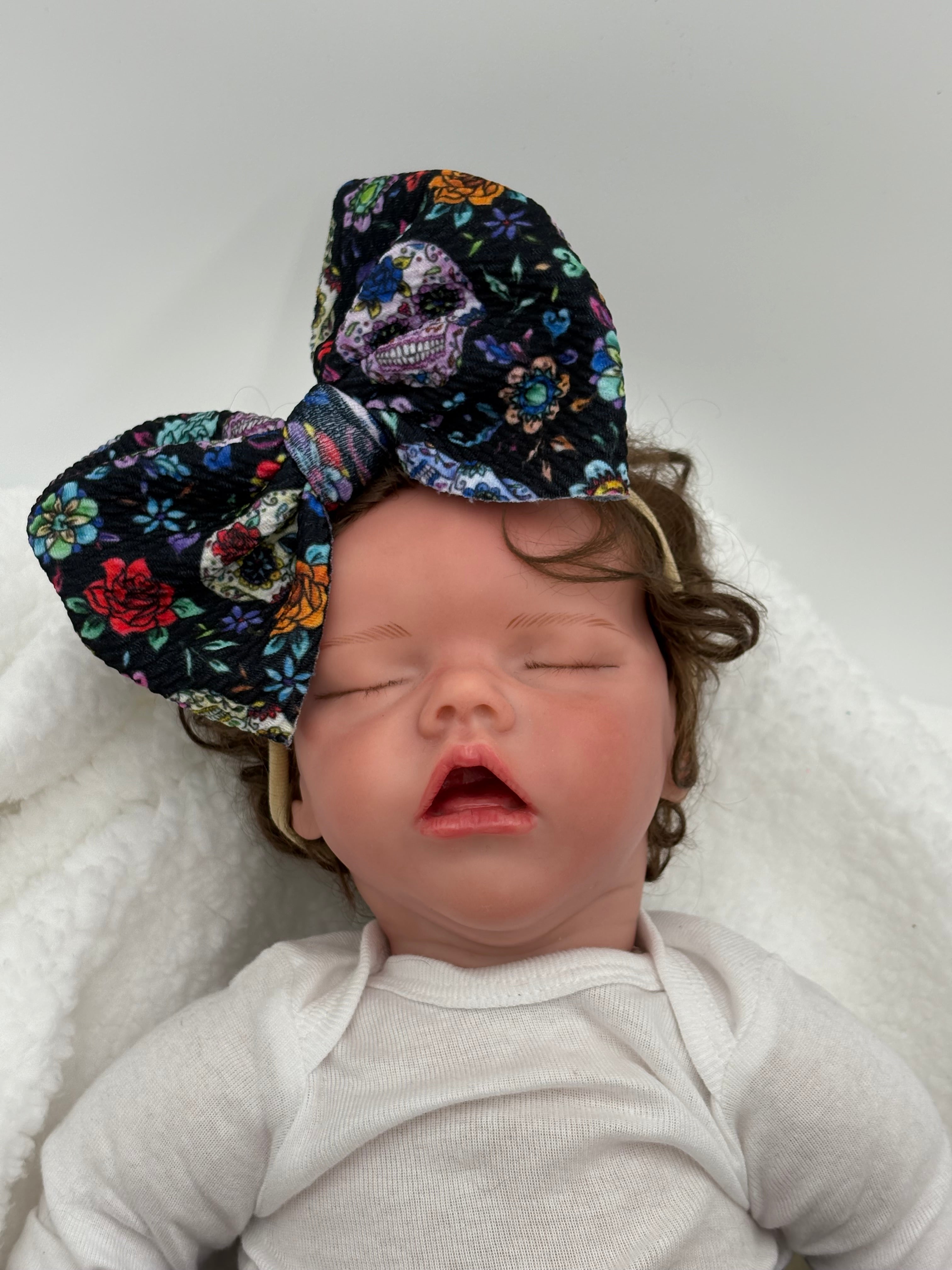 baby doll wearing a Day of the dead sugar skulls themed big bow nylon headband on a white background