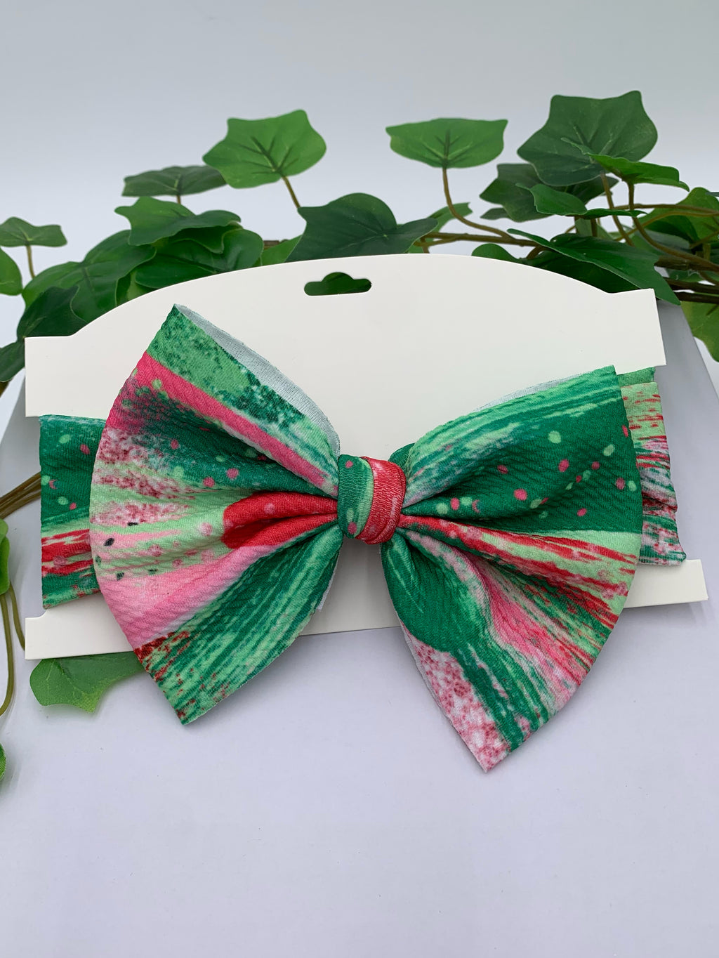 colorful big bow headband on a white card stock with white background and greenery. 