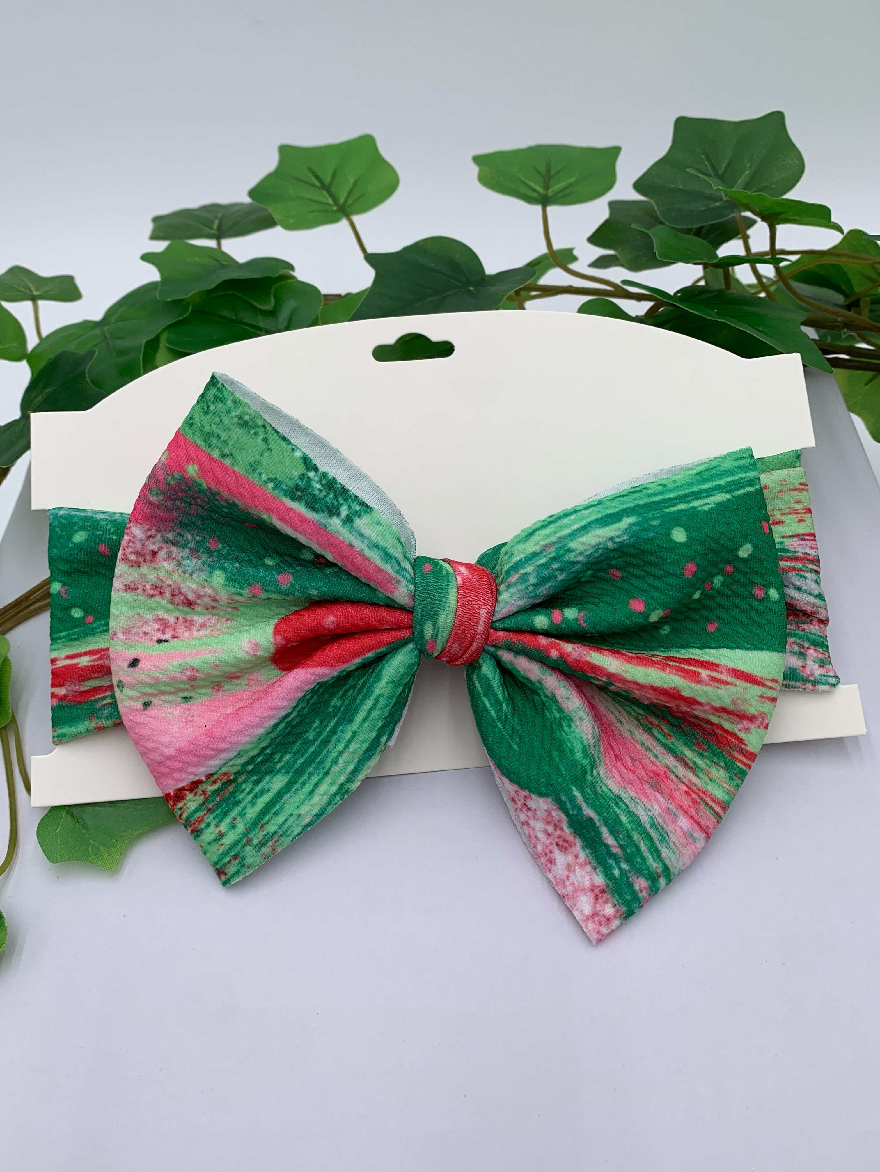colorful big bow headband on a white card stock with white background and greenery. 
