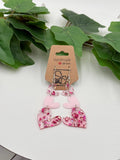 Pink heart-shaped dangle earrings on a card with green leaves in the background