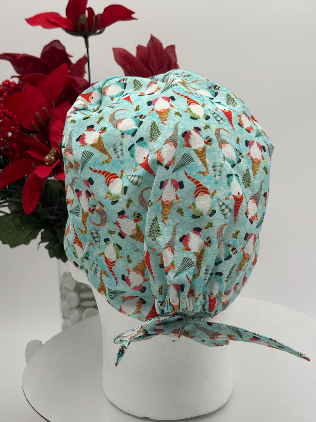 Colorful gnome pattern with baby blue background scrub cap on a mannequin head with a red floral arrangement in the background