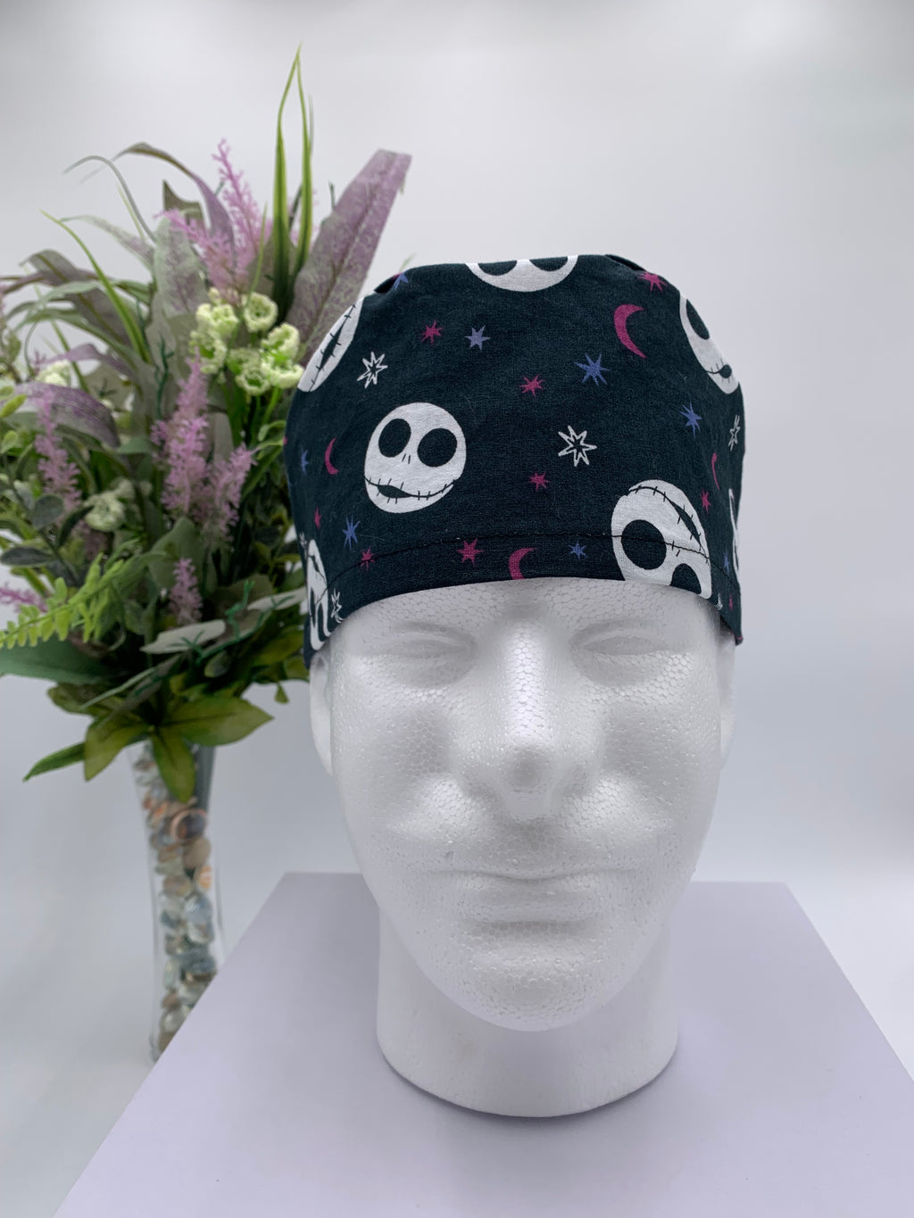 Mannequin head wearing a jack skellington scrub cap with a decorative plant in the background.