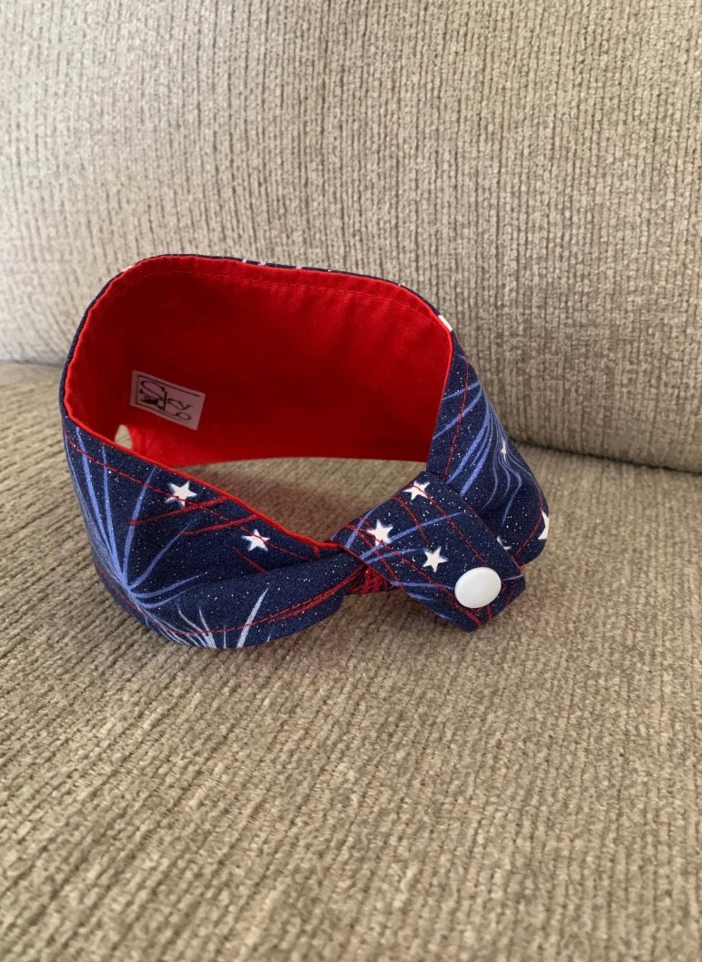 back of a tied Blue with light blue and red fireworks with white stars 4th of july themed pet bandana on a beige couch