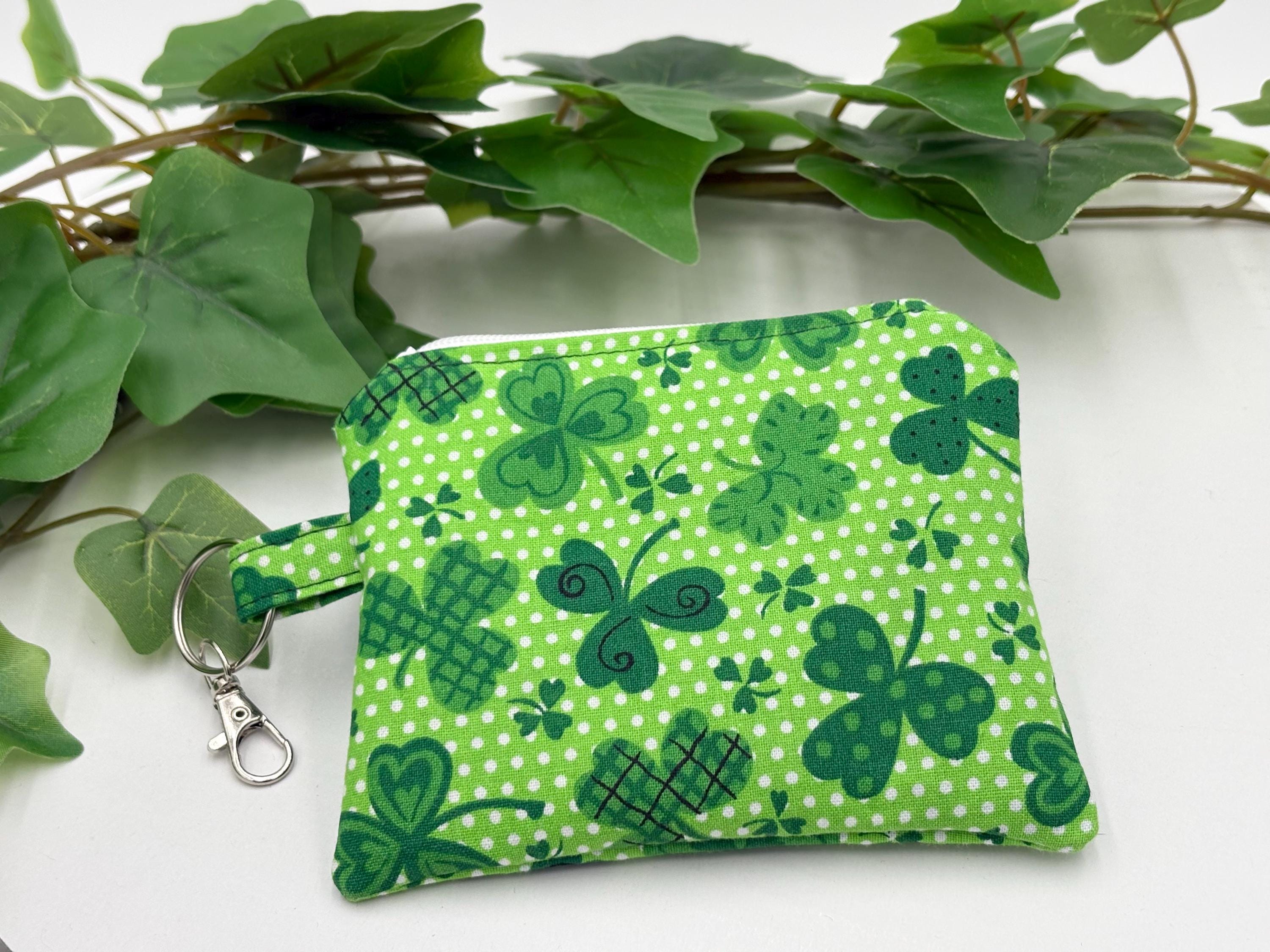 Small coin purse keychain with green shamrocks pattern on a white background with green leaves