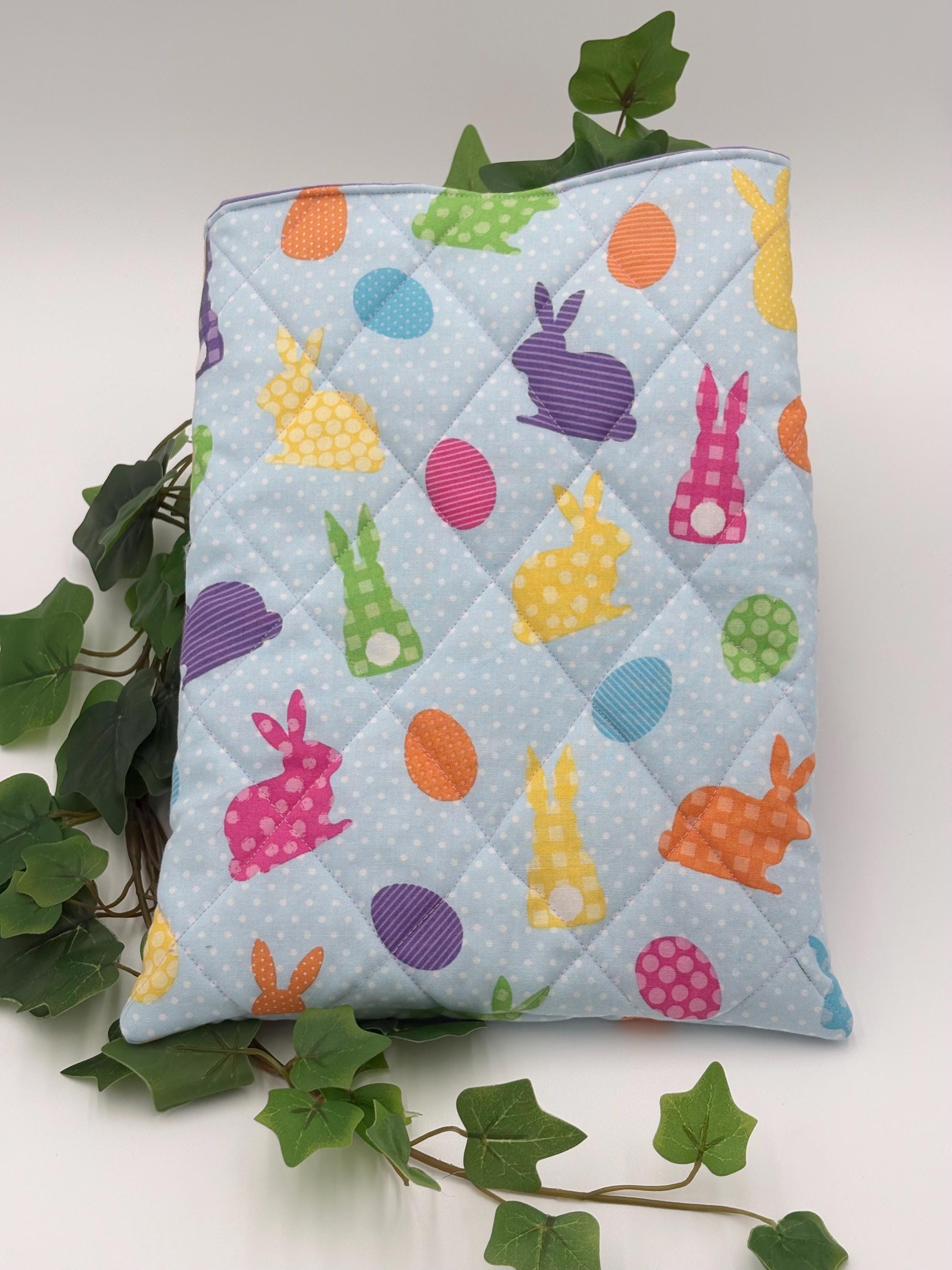 Quilted Easter-themed ipad sleeve with colorful bunnies and eggs on a light blue background, surrounded by green leaves.