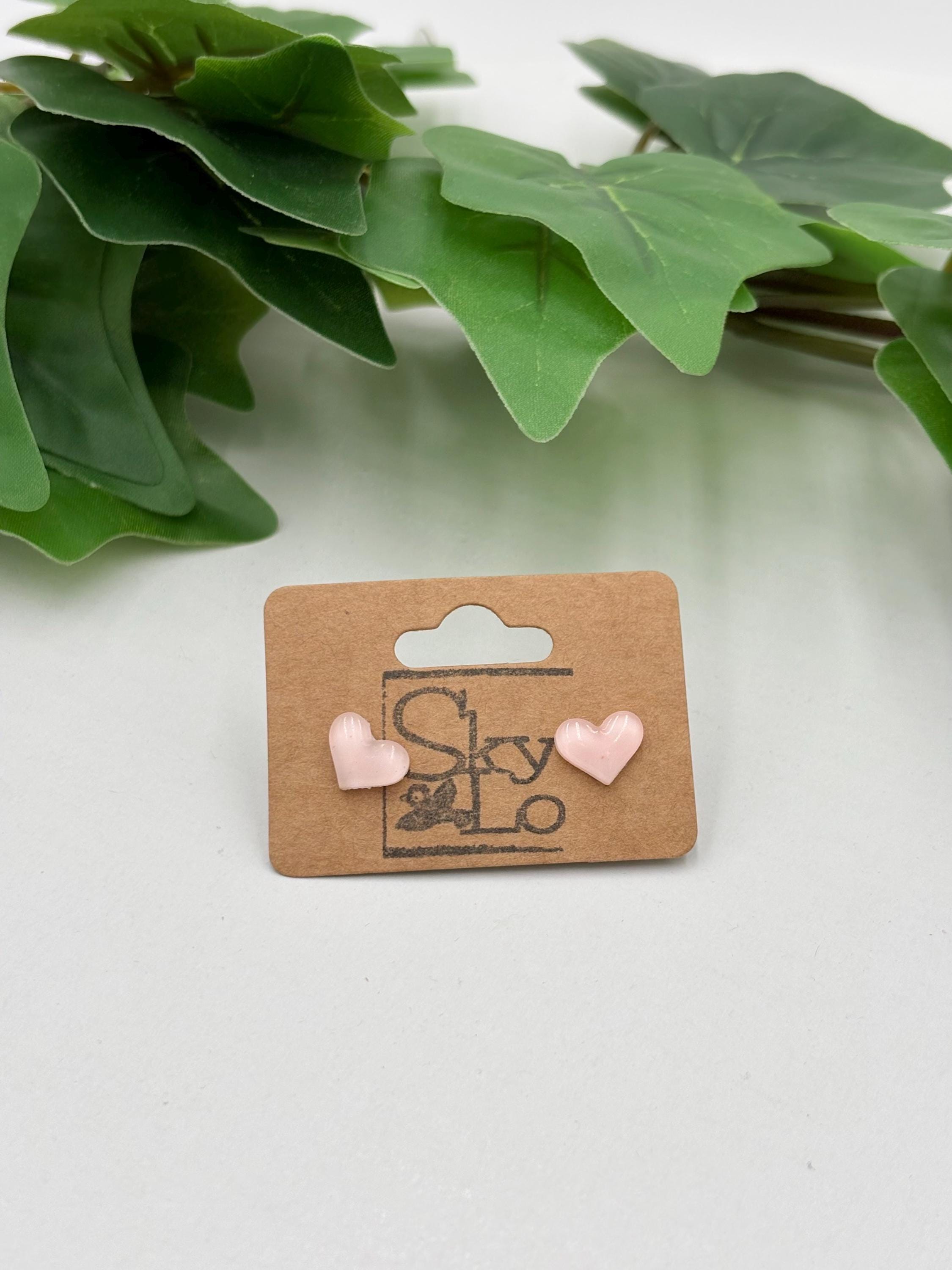 Pair of pink heart-shaped earrings on a 'SkyLo' branded card with green leaves in the background.