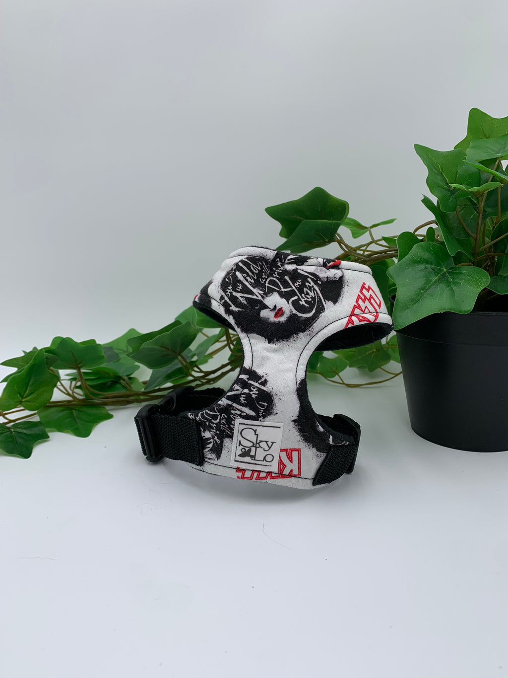A white heavy metal band pattern harness on a white background with a potted green plant