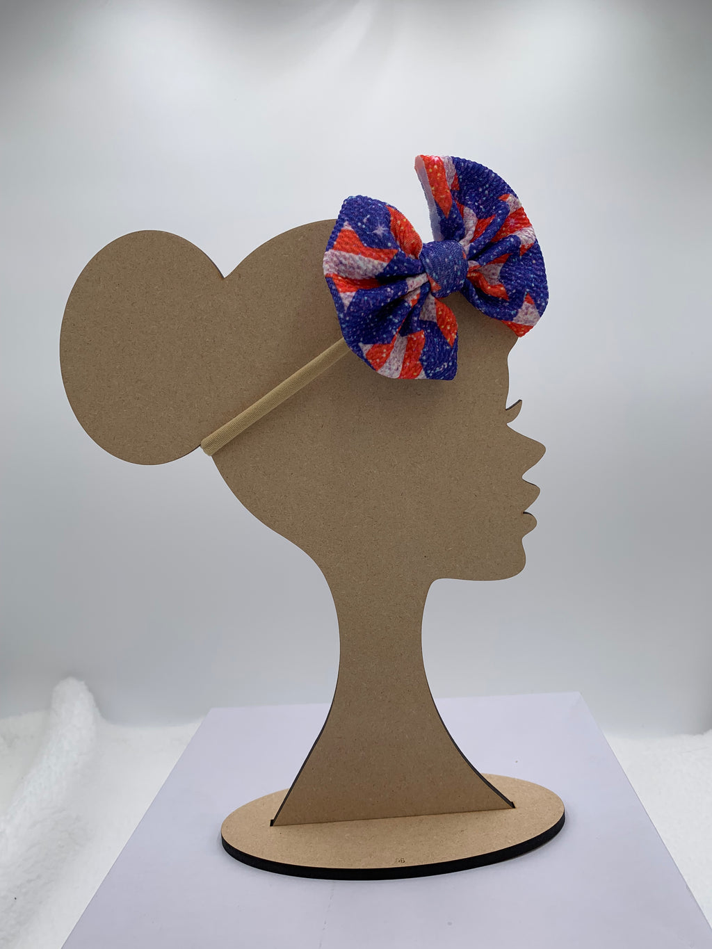 Wooden mannequin silhouette head with a 4th of july star themed bow nylon headband with white background