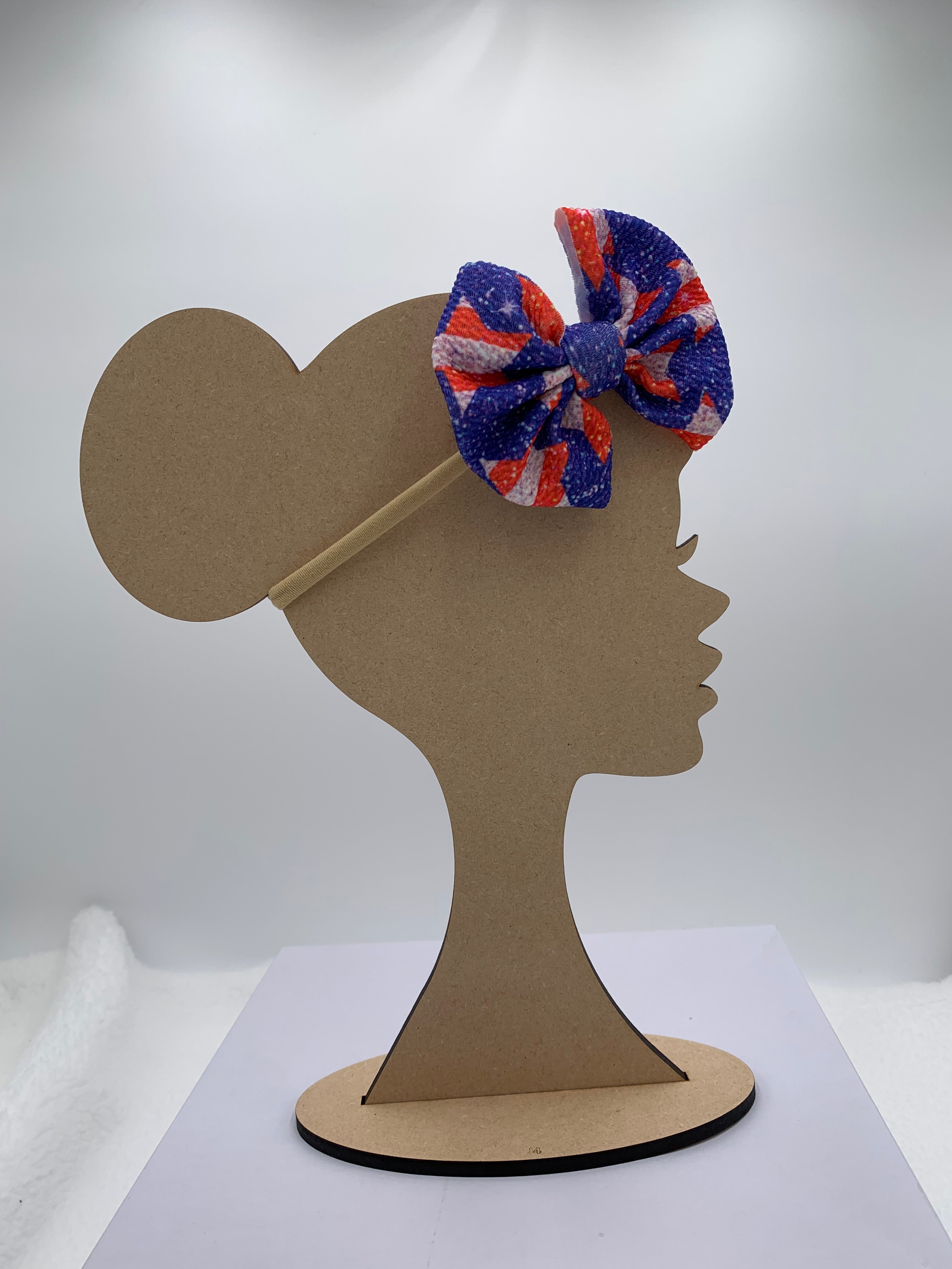 Wooden mannequin silhouette head with a 4th of july star themed bow nylon headband with white background
