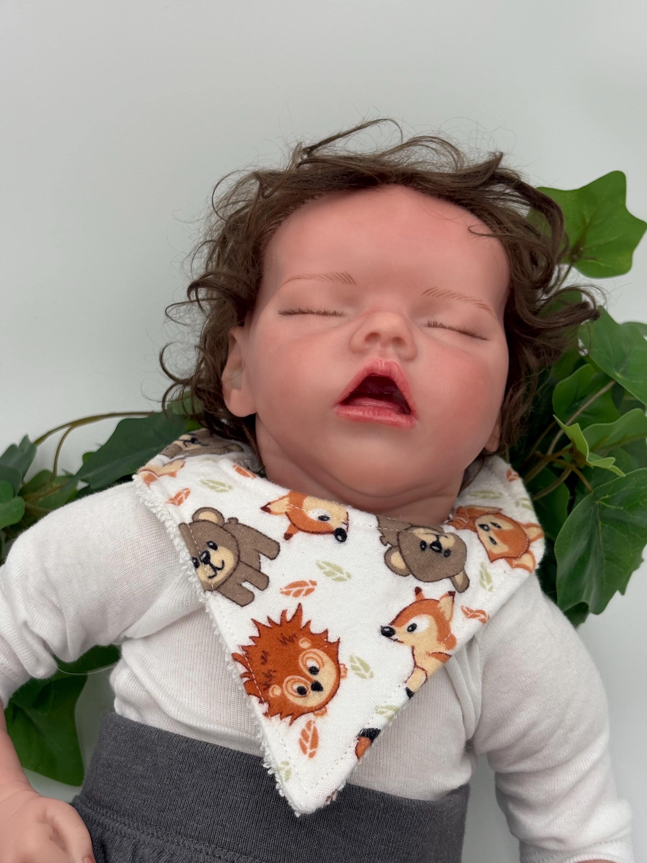 Baby doll wearing a bib with animal patterns against a green leafy background