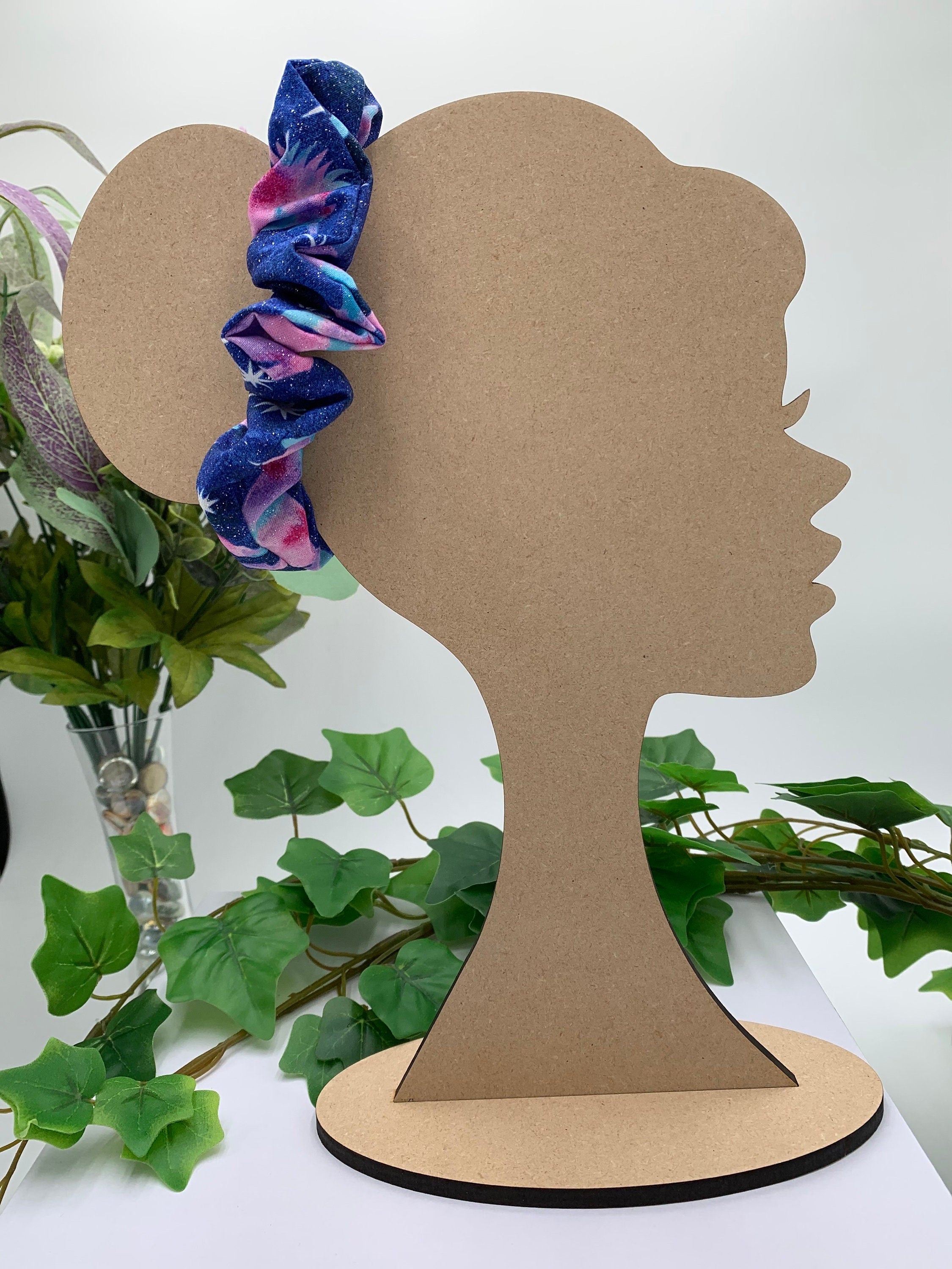 Cardboard silhouette of a head with a blue unicorn scrunchie on a white background with greenery.