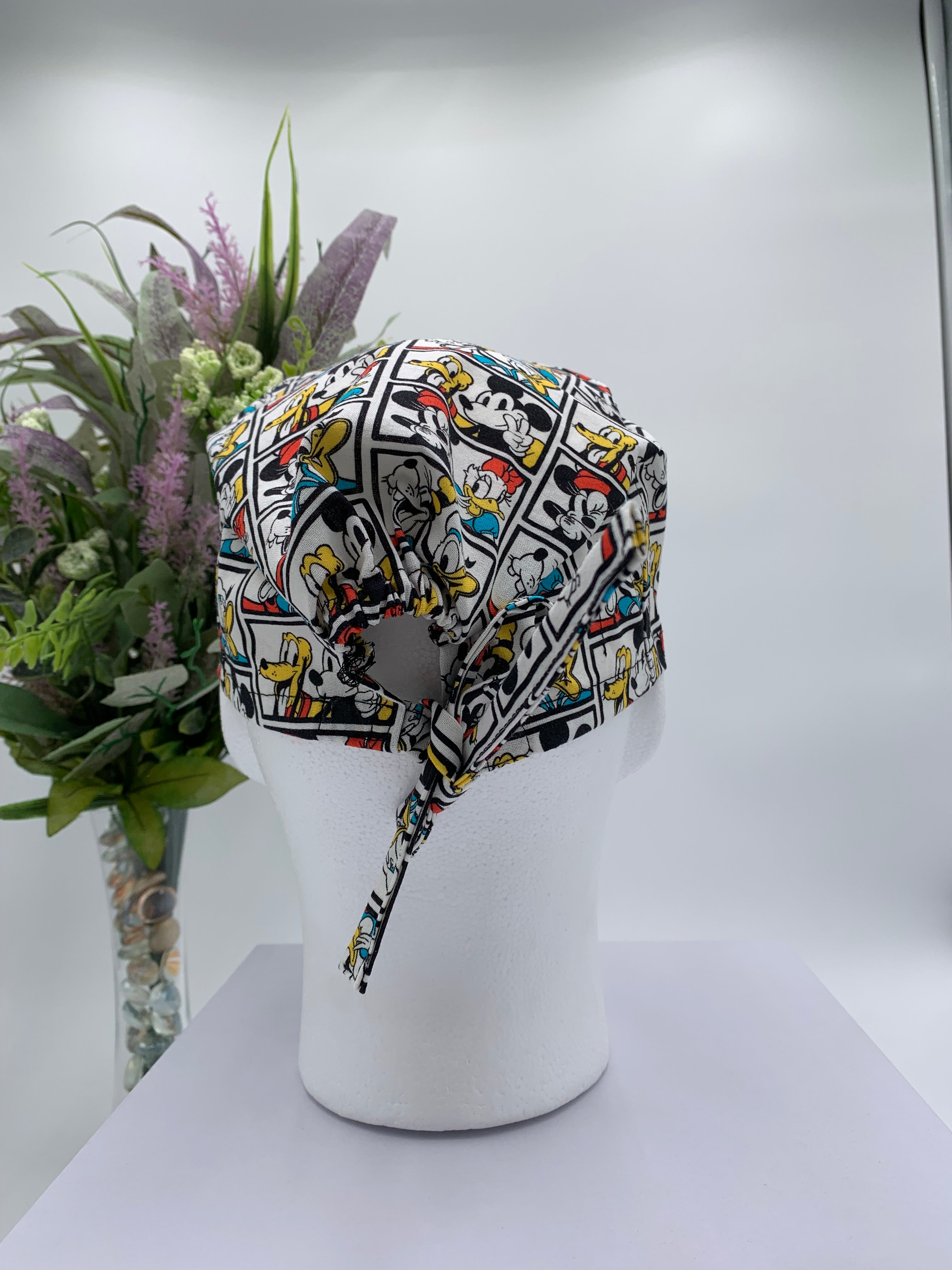 Mickey Mouse scrub cap on a mannequin head with a white background and flowers in the background