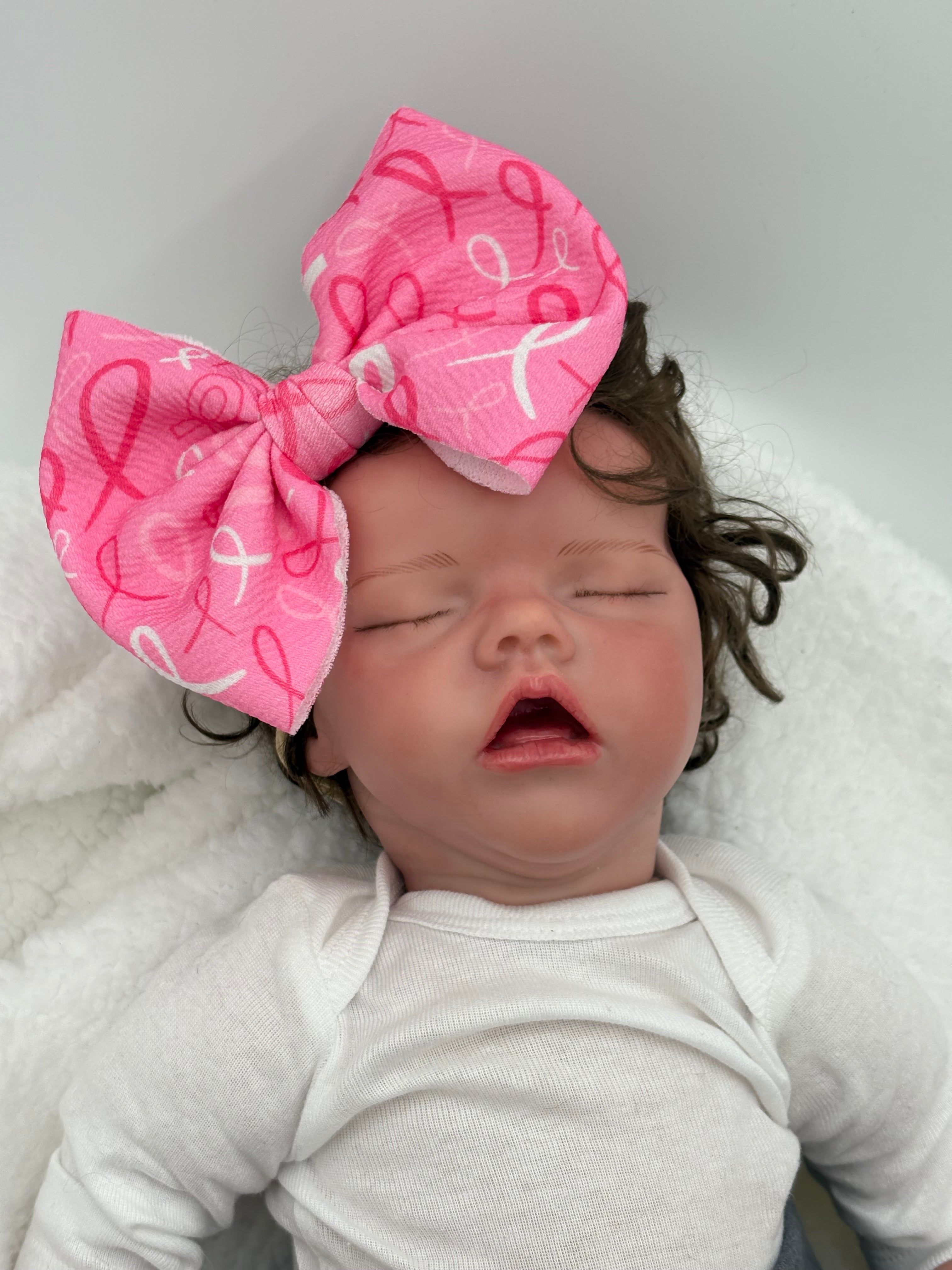 baby doll wearing a Pink Breast Cancer awareness themed big bow nylon headband on a white background 