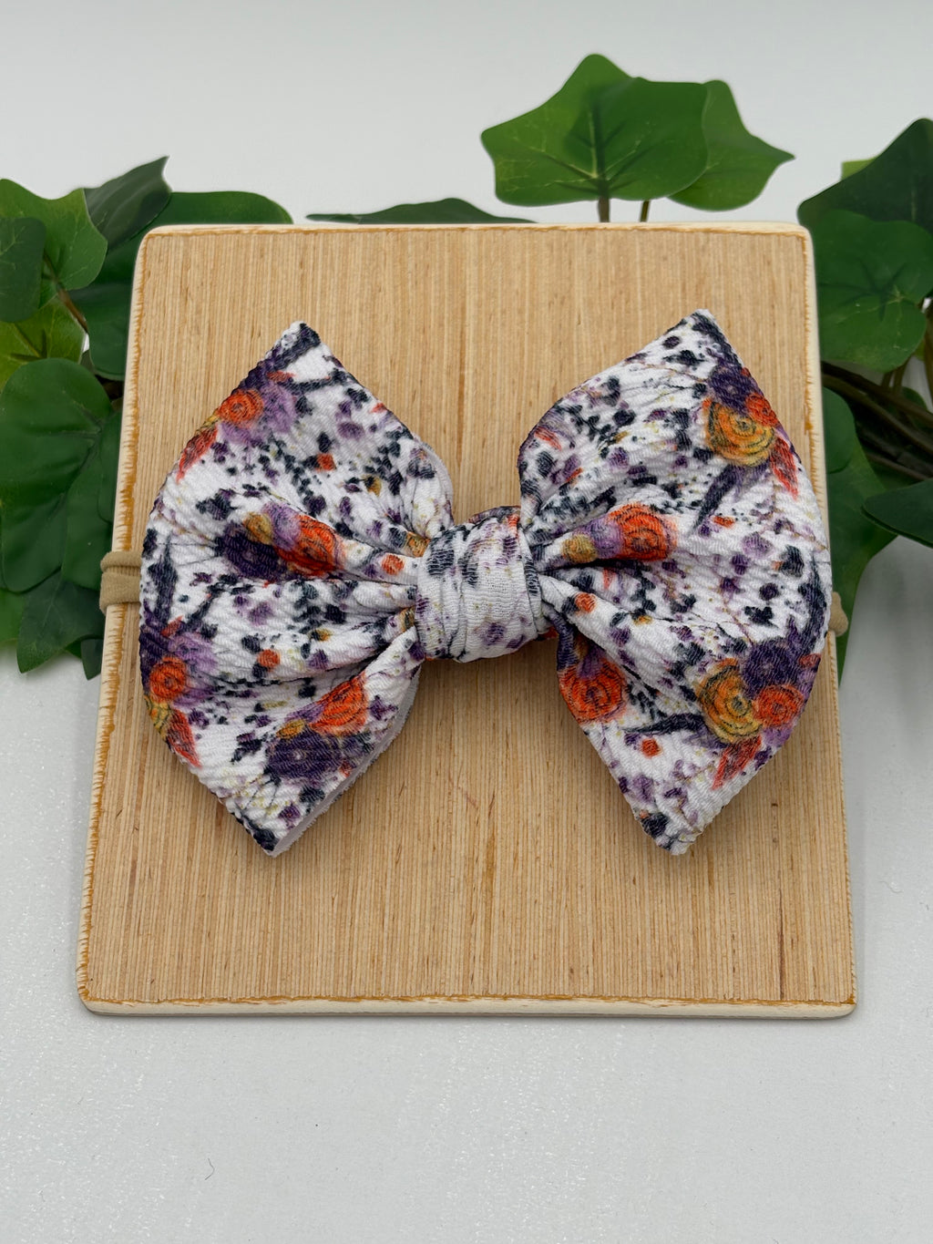 Autumn floral themed big bow nylon headband on a wooden board with a white background and greenery 