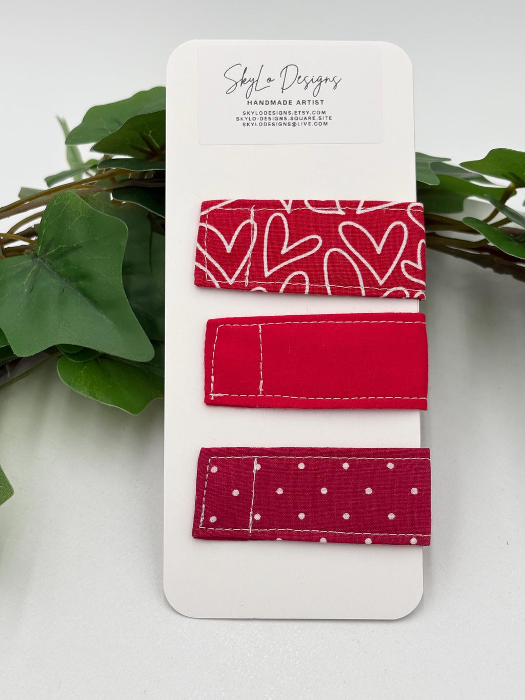Set of red magnetic bookmarks with different patterns on a white card, with green leaves in the background.