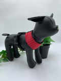 Black dog mannequin with a red polka dot harness on a white background with a ivy plant 