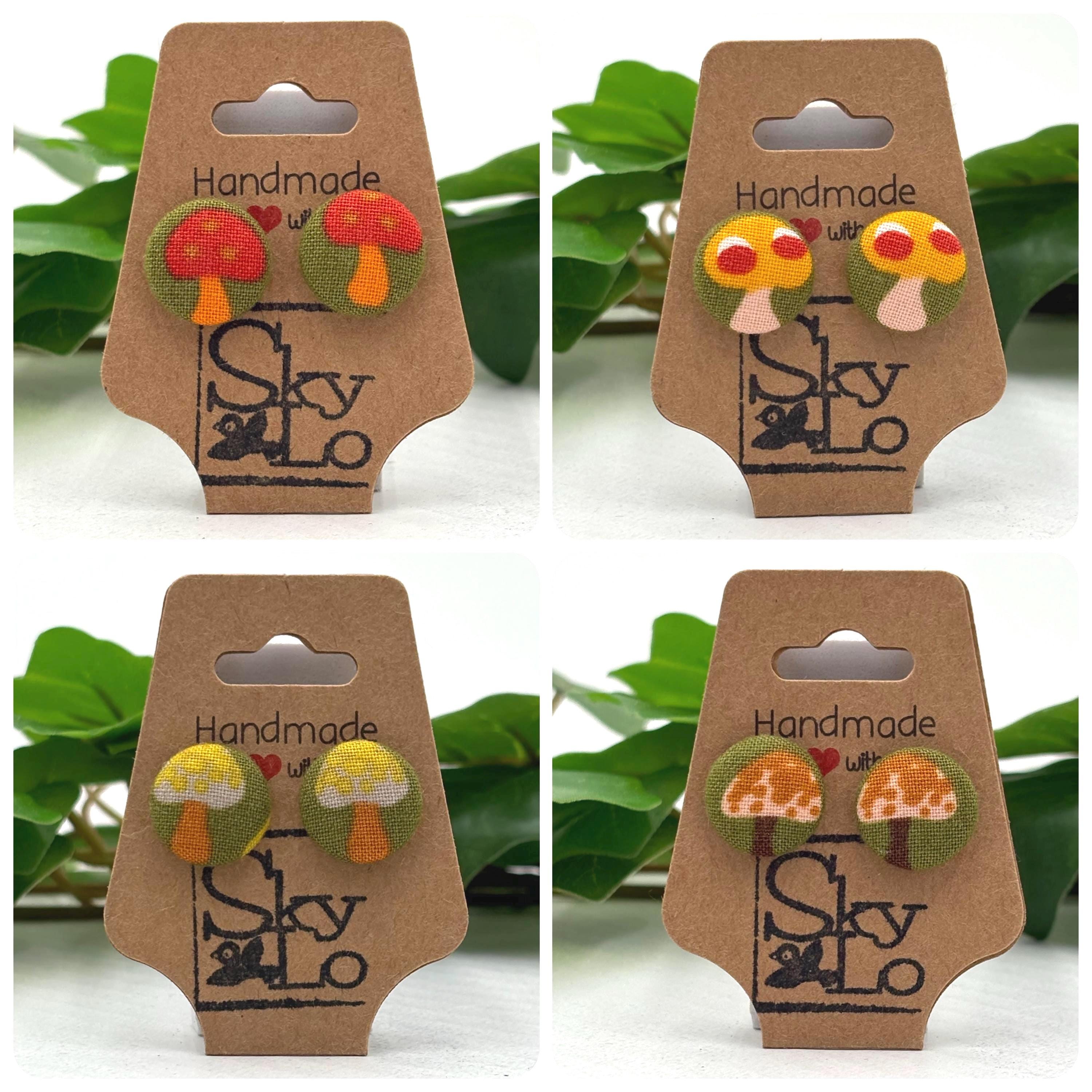Four sets of mushroom-shaped earrings on a 'Handmade with Love' and 'SkyLo' branded card against a green leafy background.