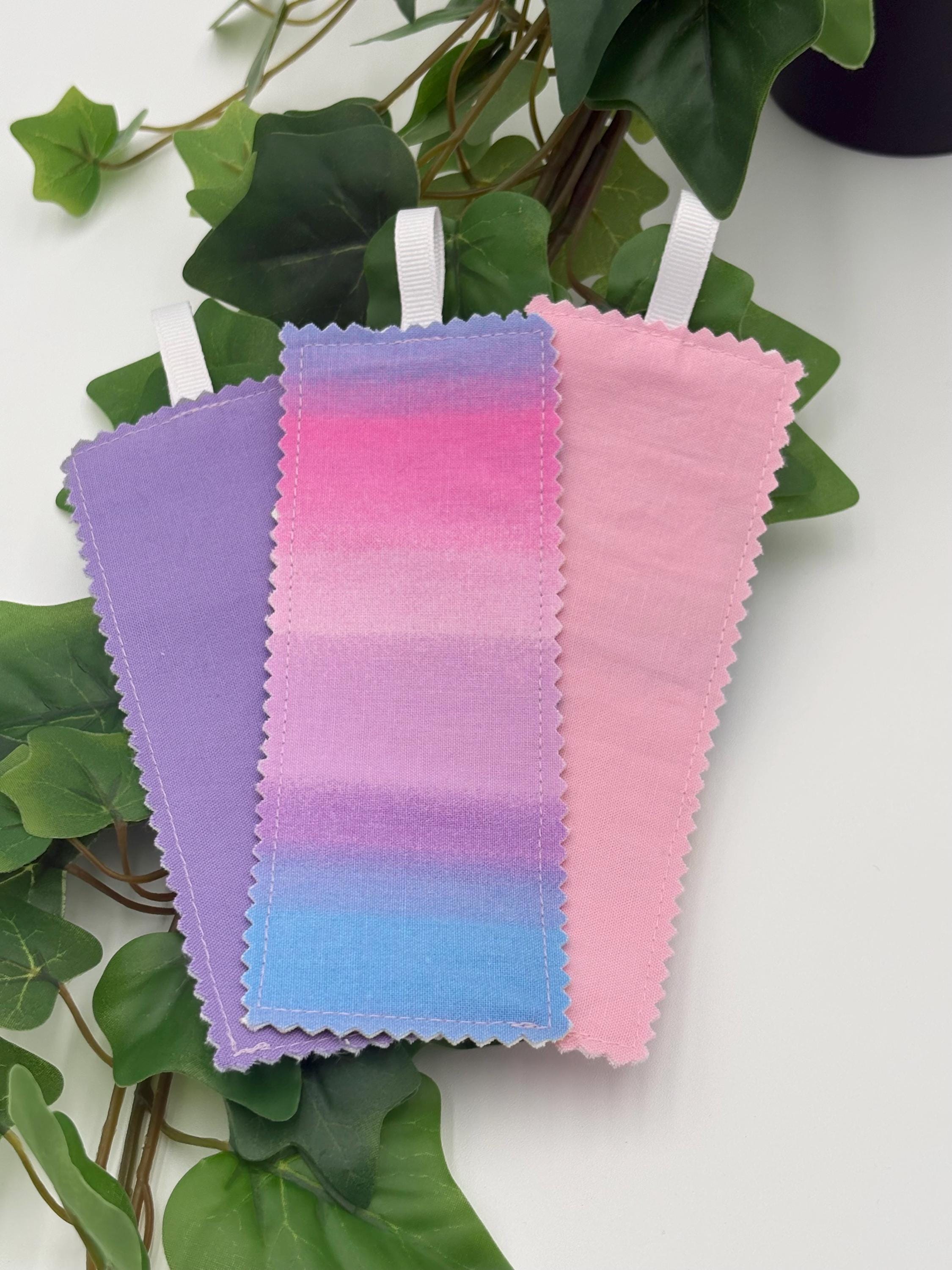 Three gradient fabric swatches in purple, pink, and blue on a green leafy background.