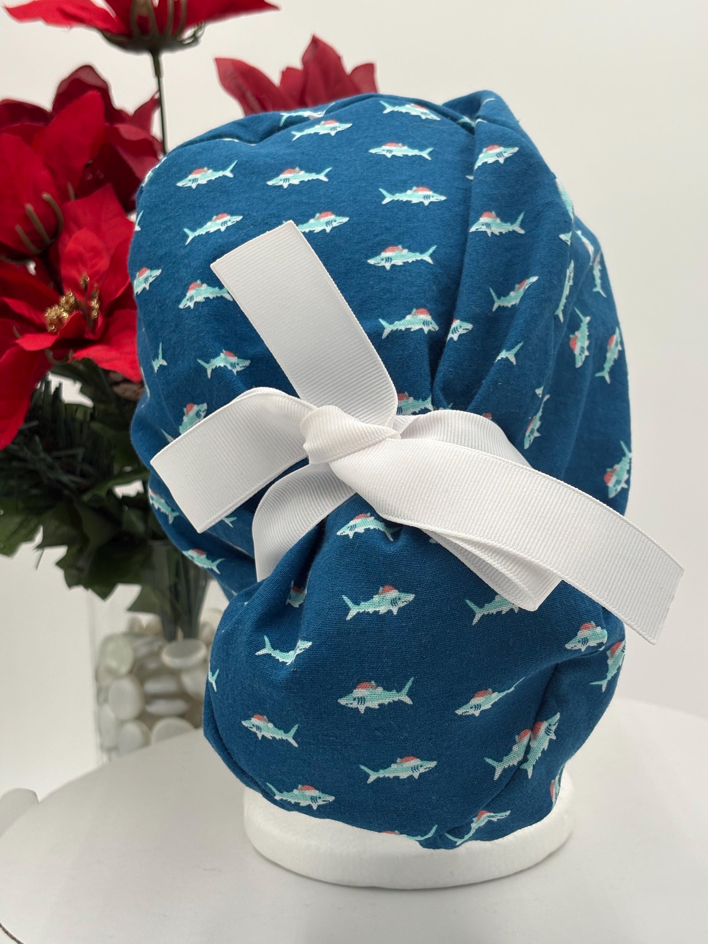 Blue Scrub cap with shark pattern on a mannequin head against a white background with red flowers