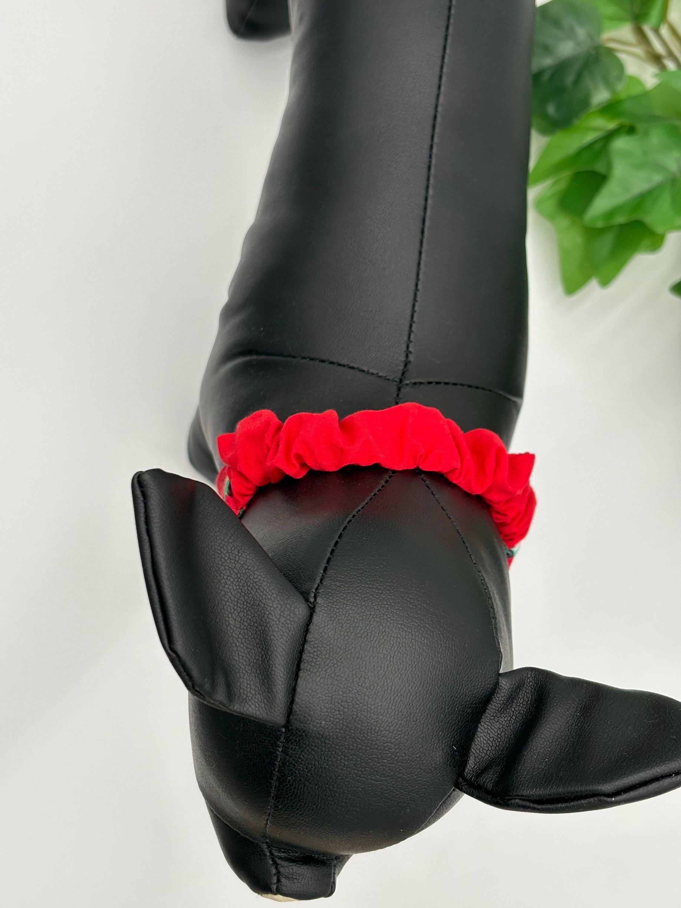 Birdseye view of Black dog mannequin with a red scrunchie bandana on a white background standing next to a potted plant. 