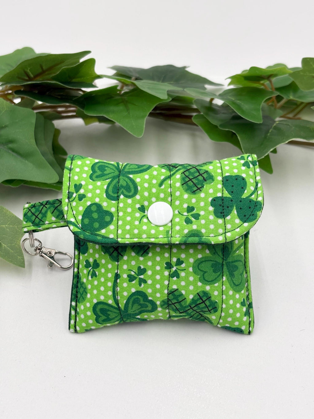 Small quilted headphone holder pouch keychain with green shamrocks design on a white surface with green leaves.
