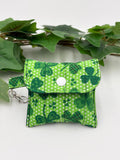 Small quilted headphone holder pouch keychain with green shamrocks design on a white surface with green leaves.