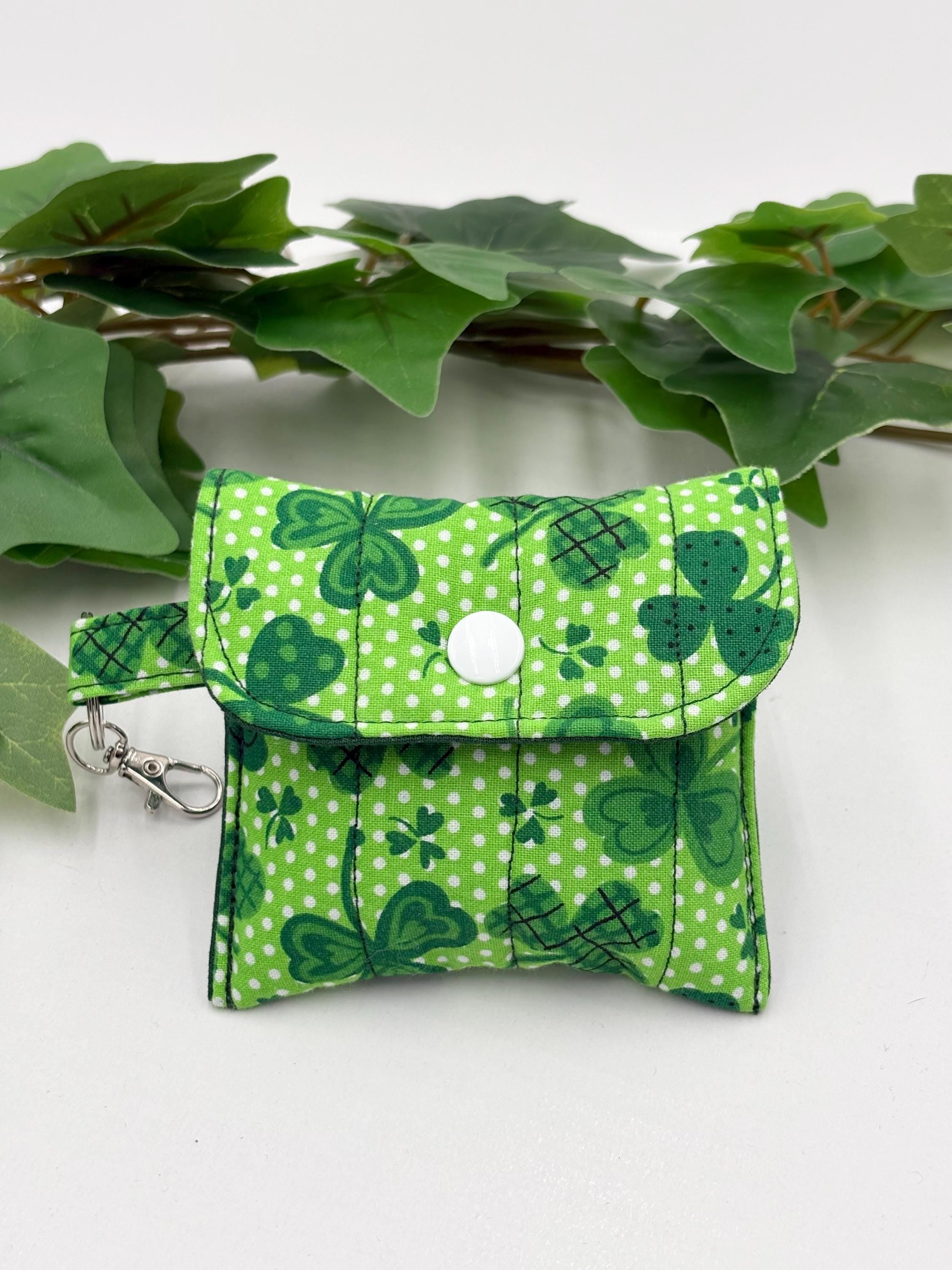 Small quilted headphone holder pouch keychain with green shamrocks design on a white surface with green leaves.