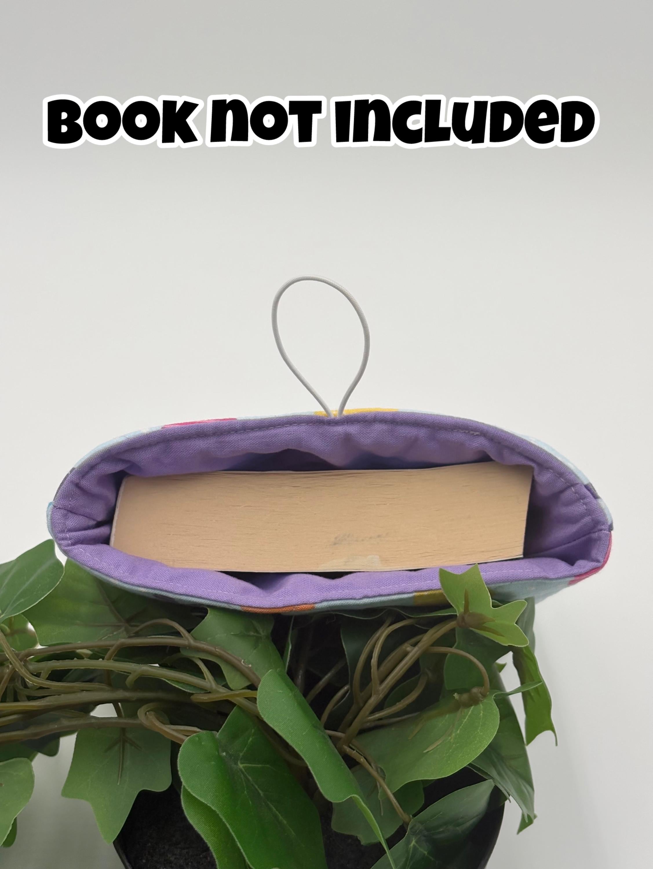 Purple book holder with a book inside, on a plant against a white background. with text "book not included".
