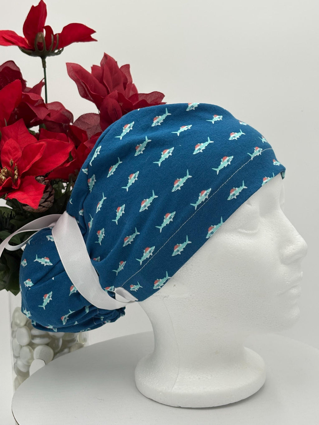 Blue Scrub cap with shark pattern on a mannequin head against a white background with red flowers