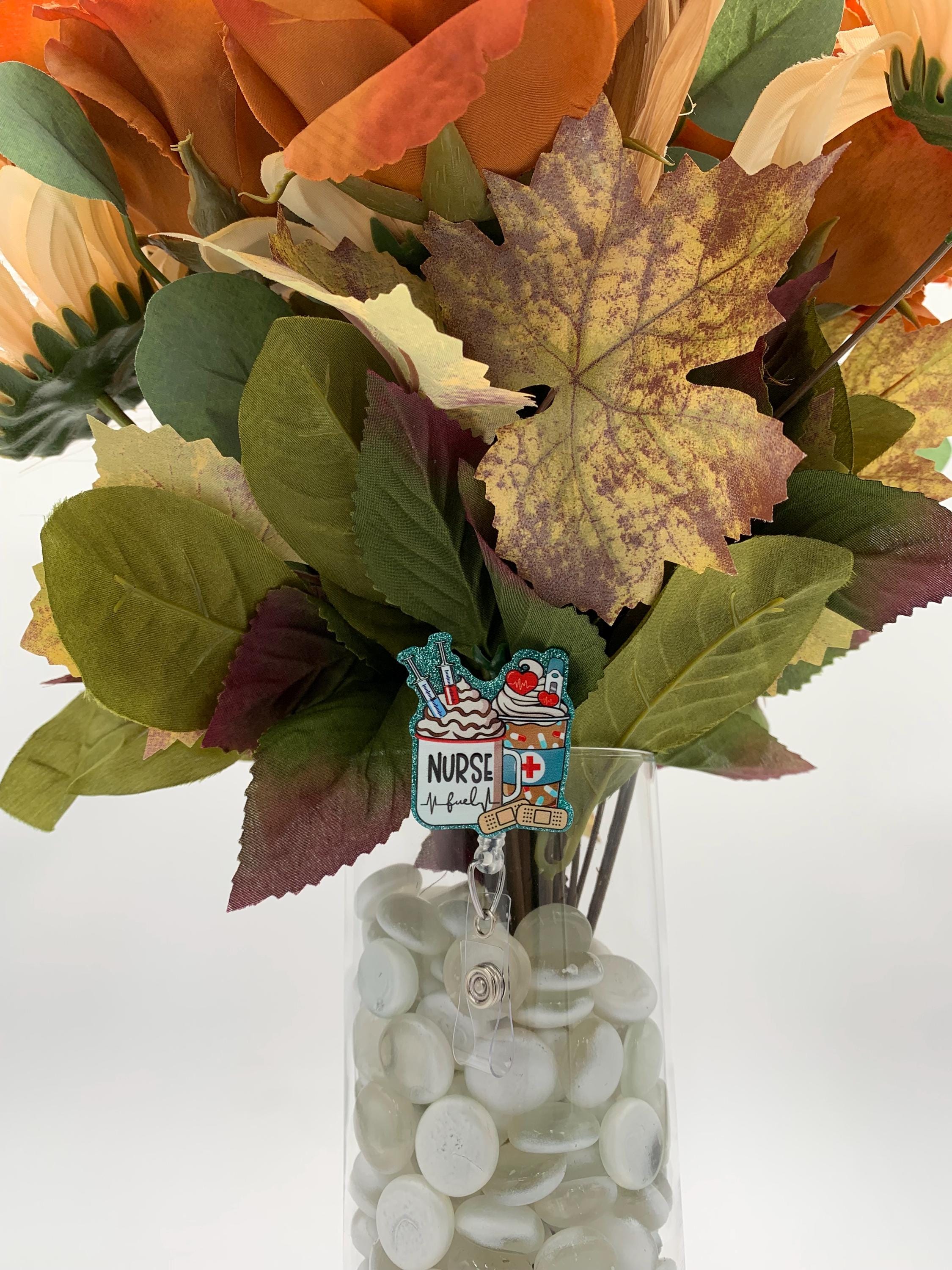 Bouquet of autumn leaves with a 'Coffee and Nurse' badge reel on a vase on a white background