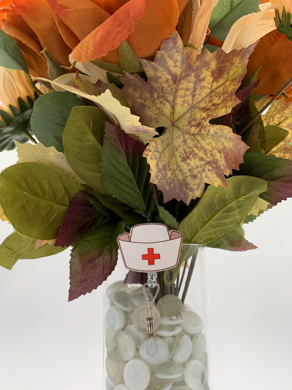 Bouquet of autumn leaves with a nurse's hat badge reel on a vase on a white background