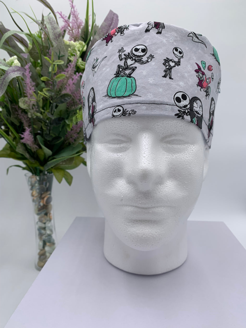 Mannequin head wearing a nightmare before christmas scrub cap with a decorative plant in the background.