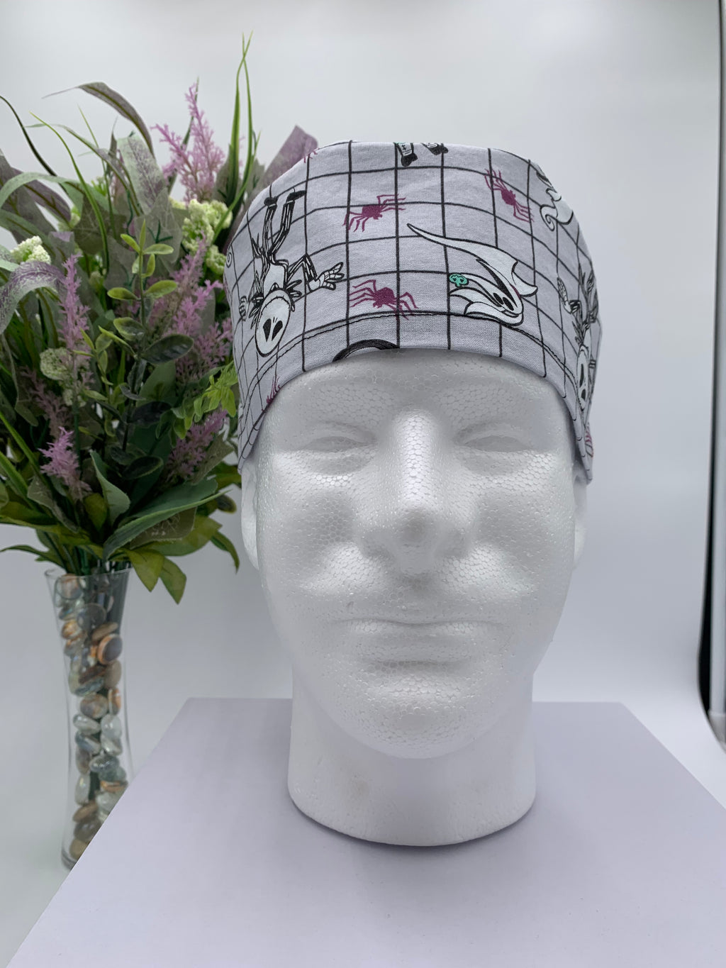 Mannequin head wearing a nightmare before christmas scrub cap with a decorative plant in the background.