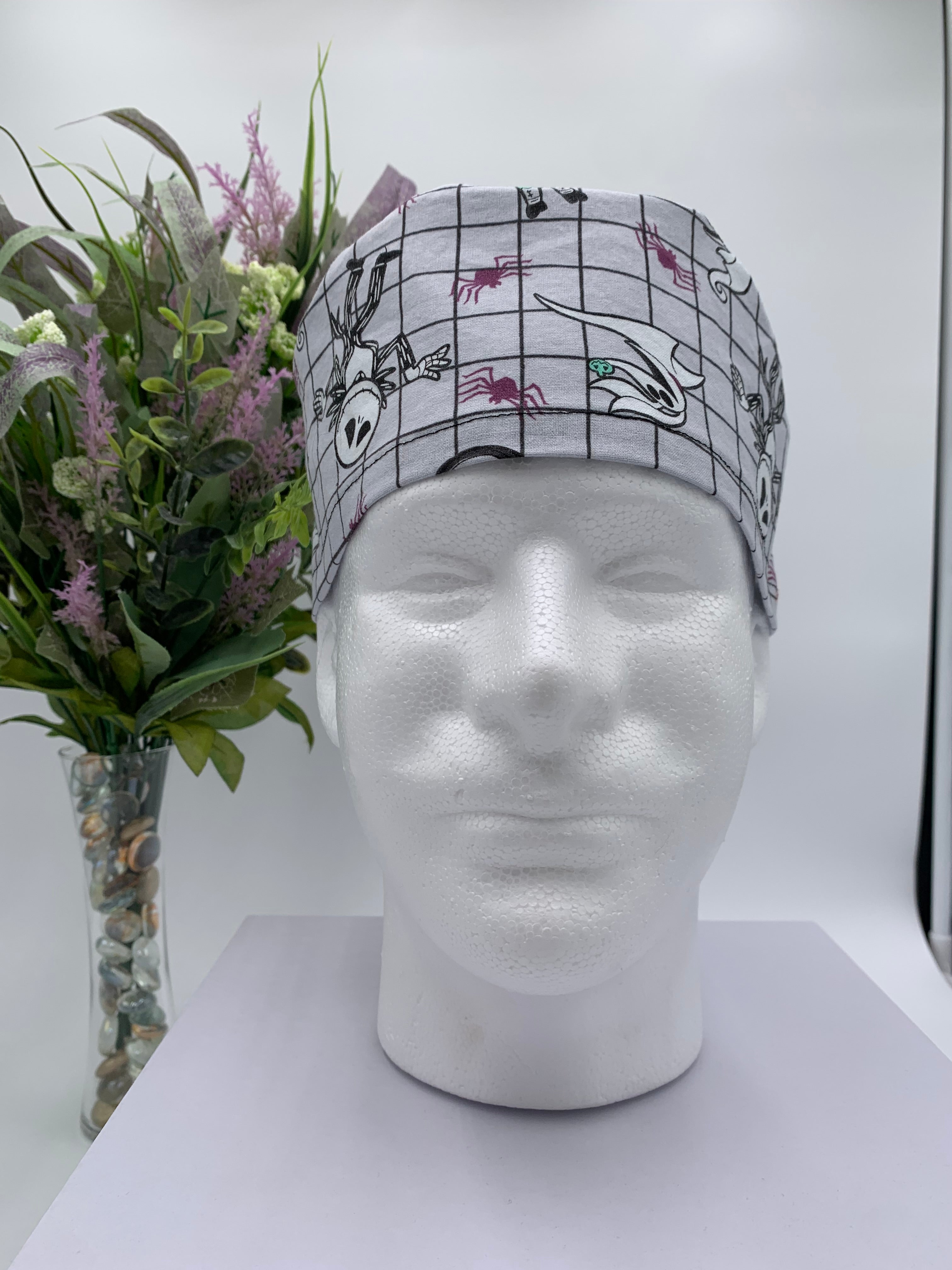 Mannequin head wearing a nightmare before christmas scrub cap with a decorative plant in the background.
